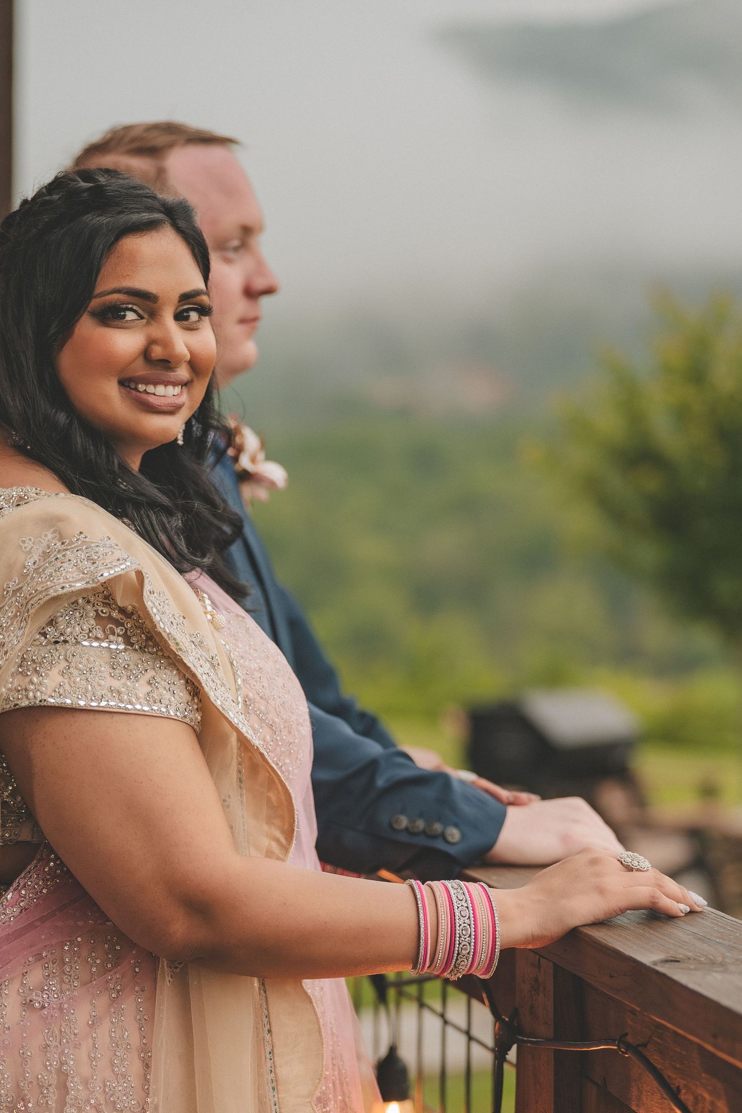 Couple enjoying scenic mountain views from wooden railing at outdoor venue in formal attire.