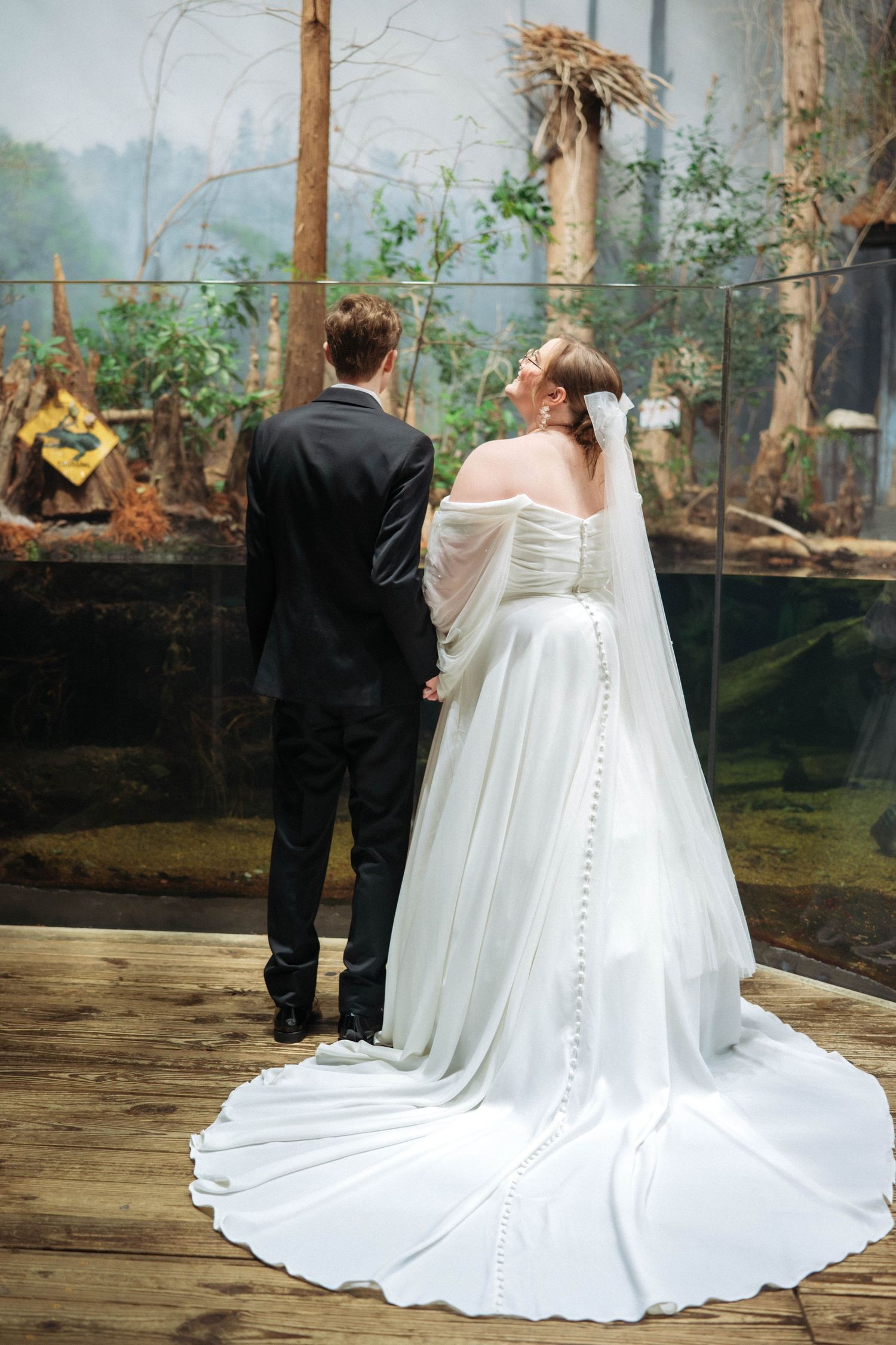 Elegant wedding couple stands on a wooden deck overlooking a misty natural backdrop.
