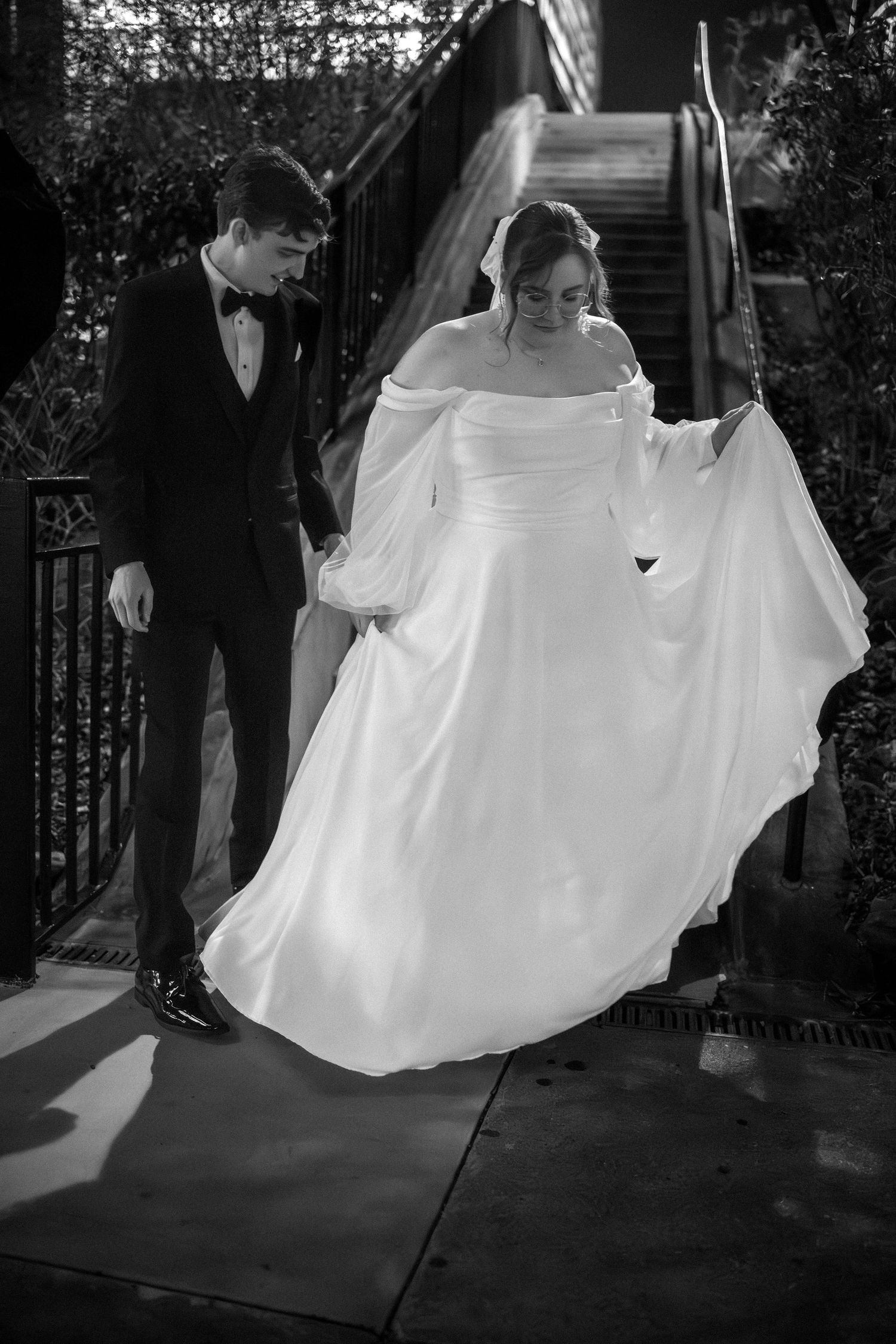 A black and white wedding photo showing a couple on outdoor steps, with the bride in a flowing white dress.