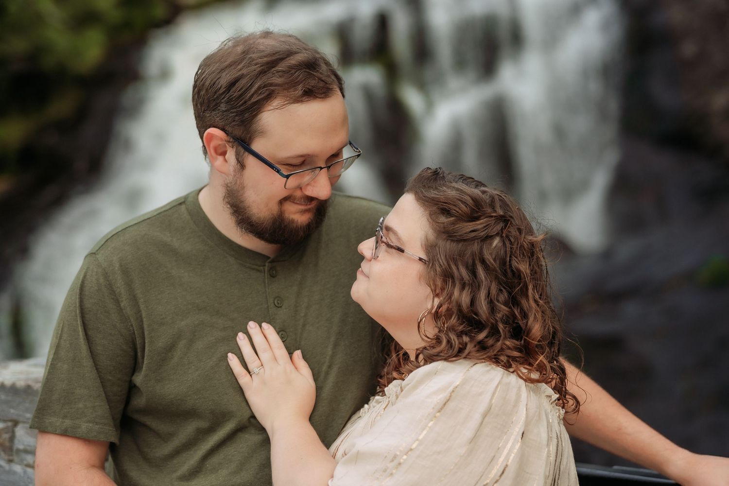 A romantic couple in coordinated outfits embraces in front of scenic waterfalls for engagement photos.