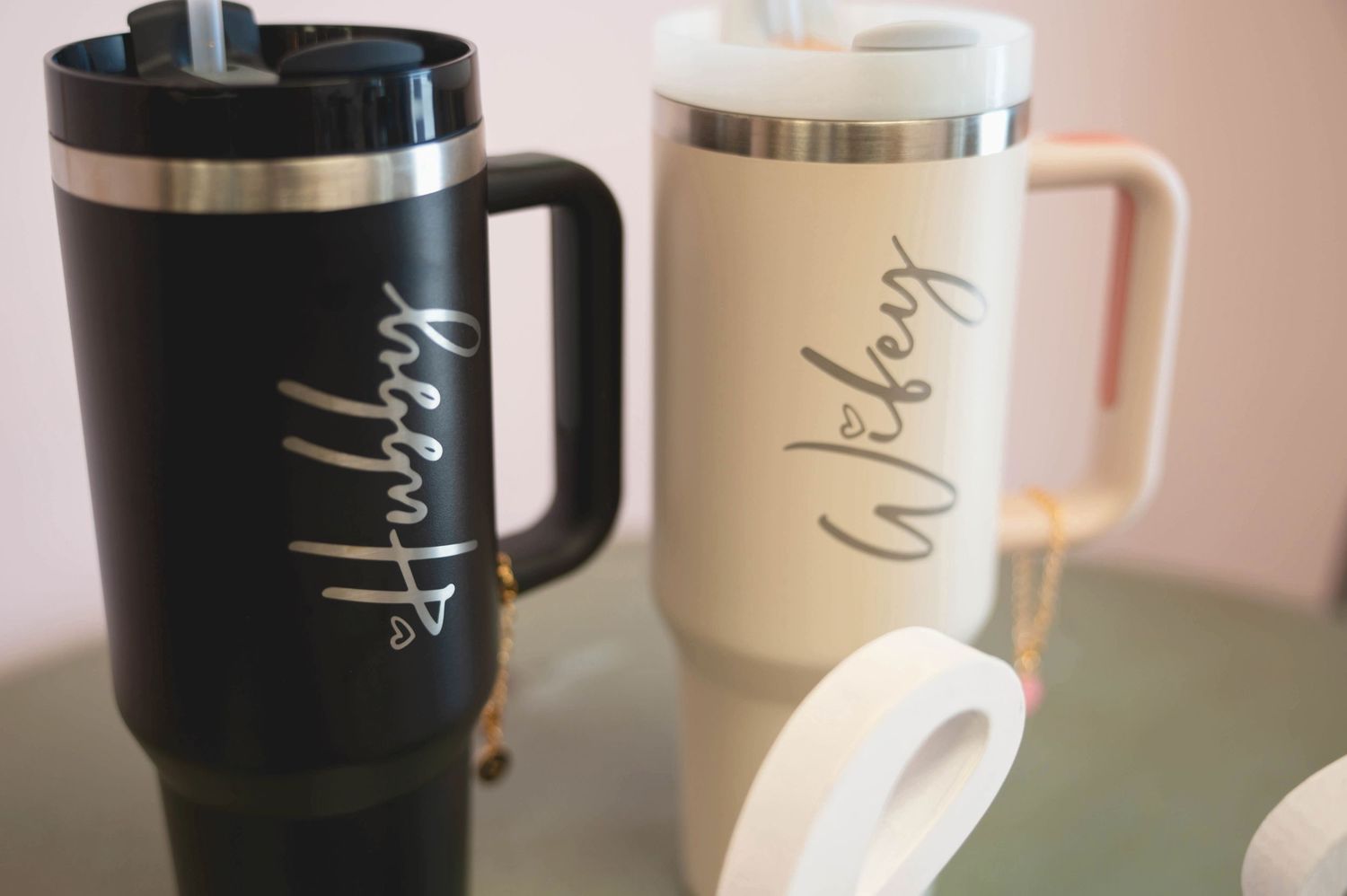 Two insulated travel mugs in black and cream colors with script text displayed on a table.