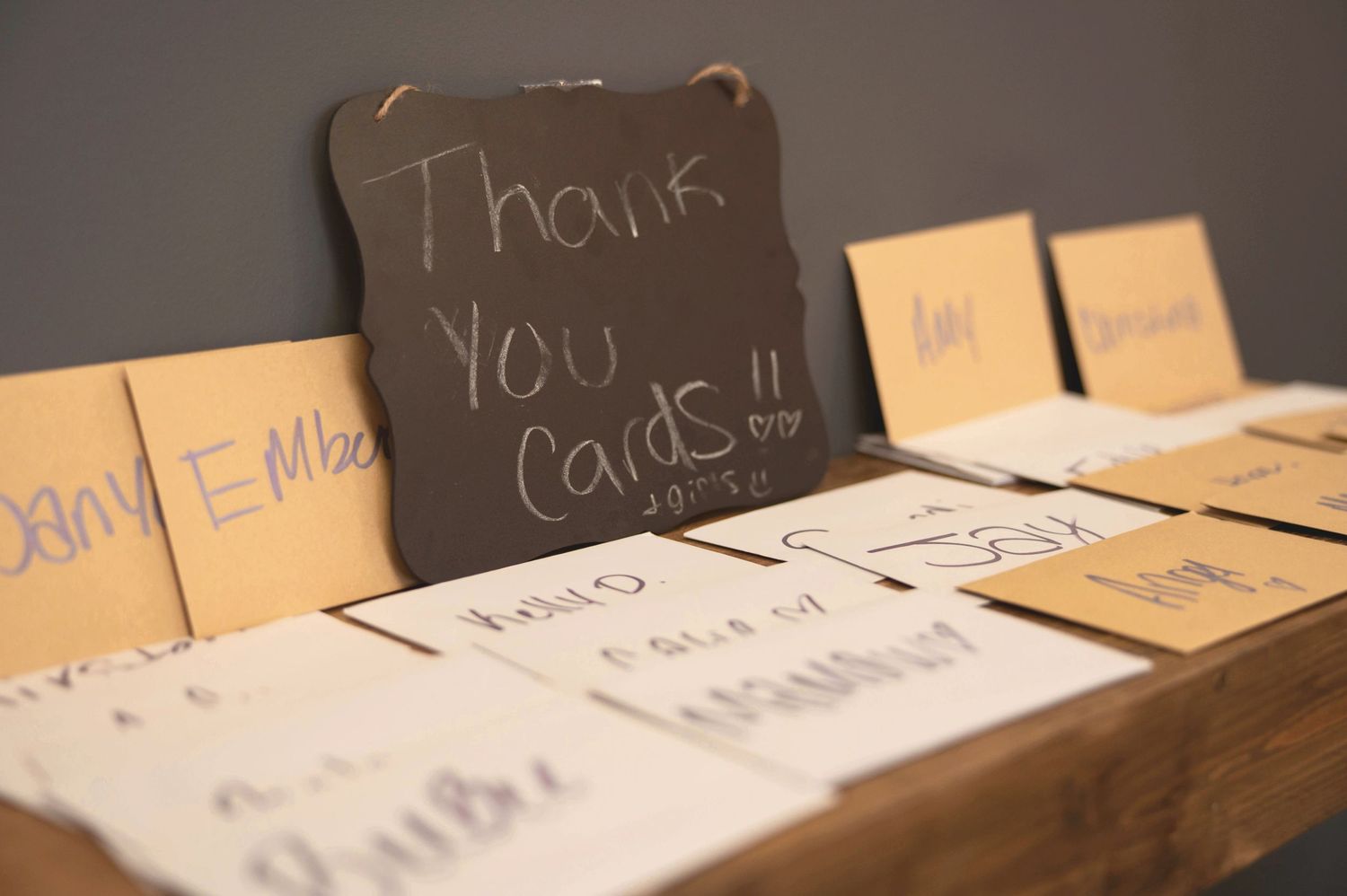 Handwritten thank you cards and notes arranged on wooden surface with chalkboard sign.