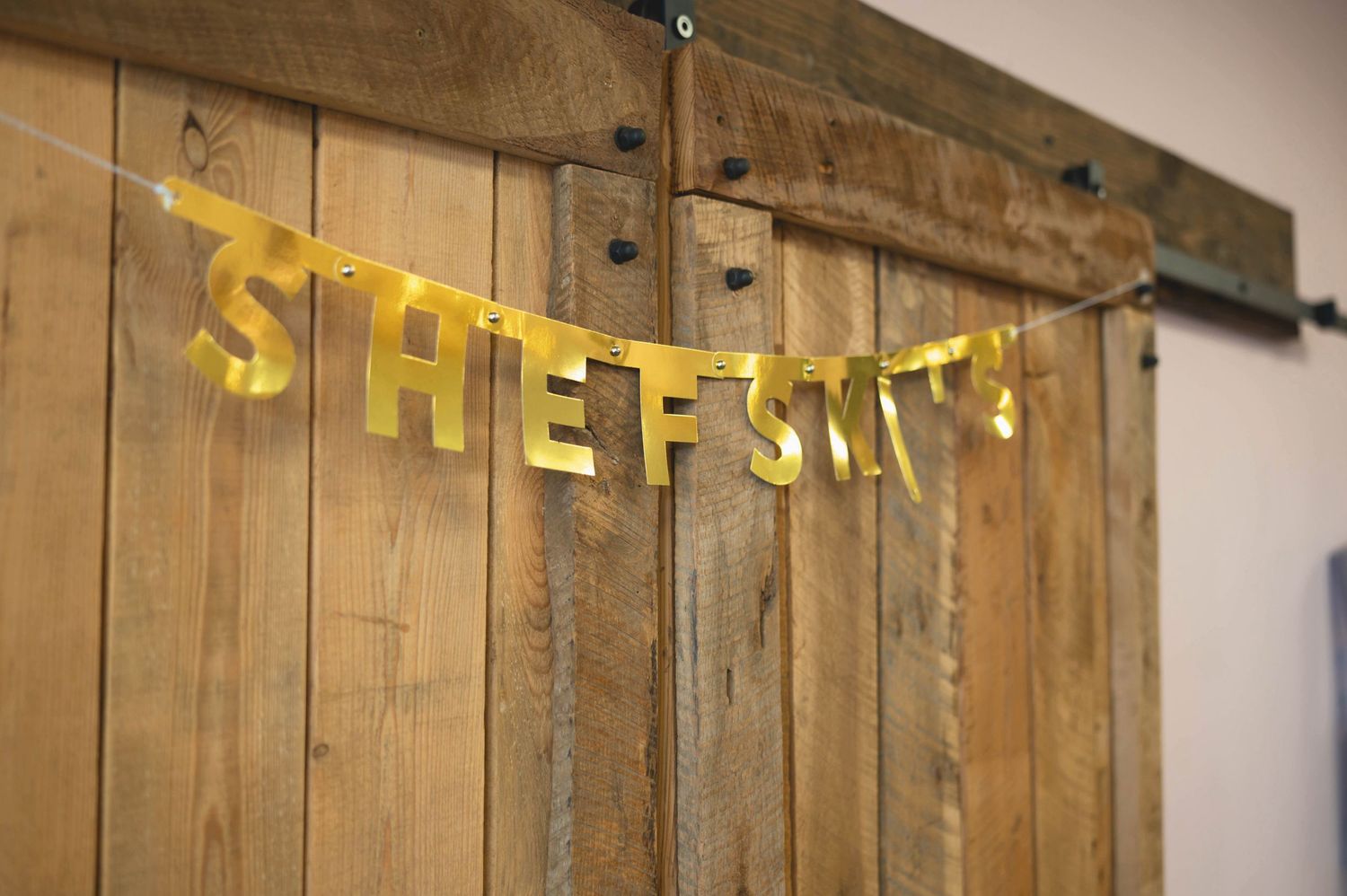 Yellow letter banner spelling 'SHEF'S' hanging on rustic wooden door or panel in warm lighting.