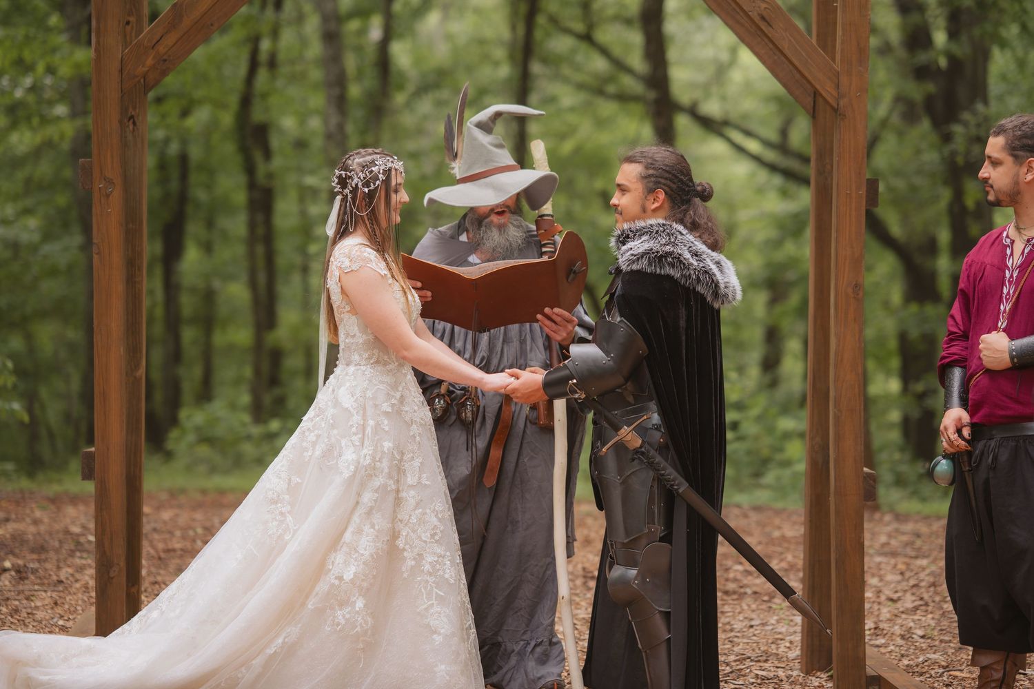 A couple shares a romantic dance in a rustic outdoor woodland setting framed by wooden beams and green trees.