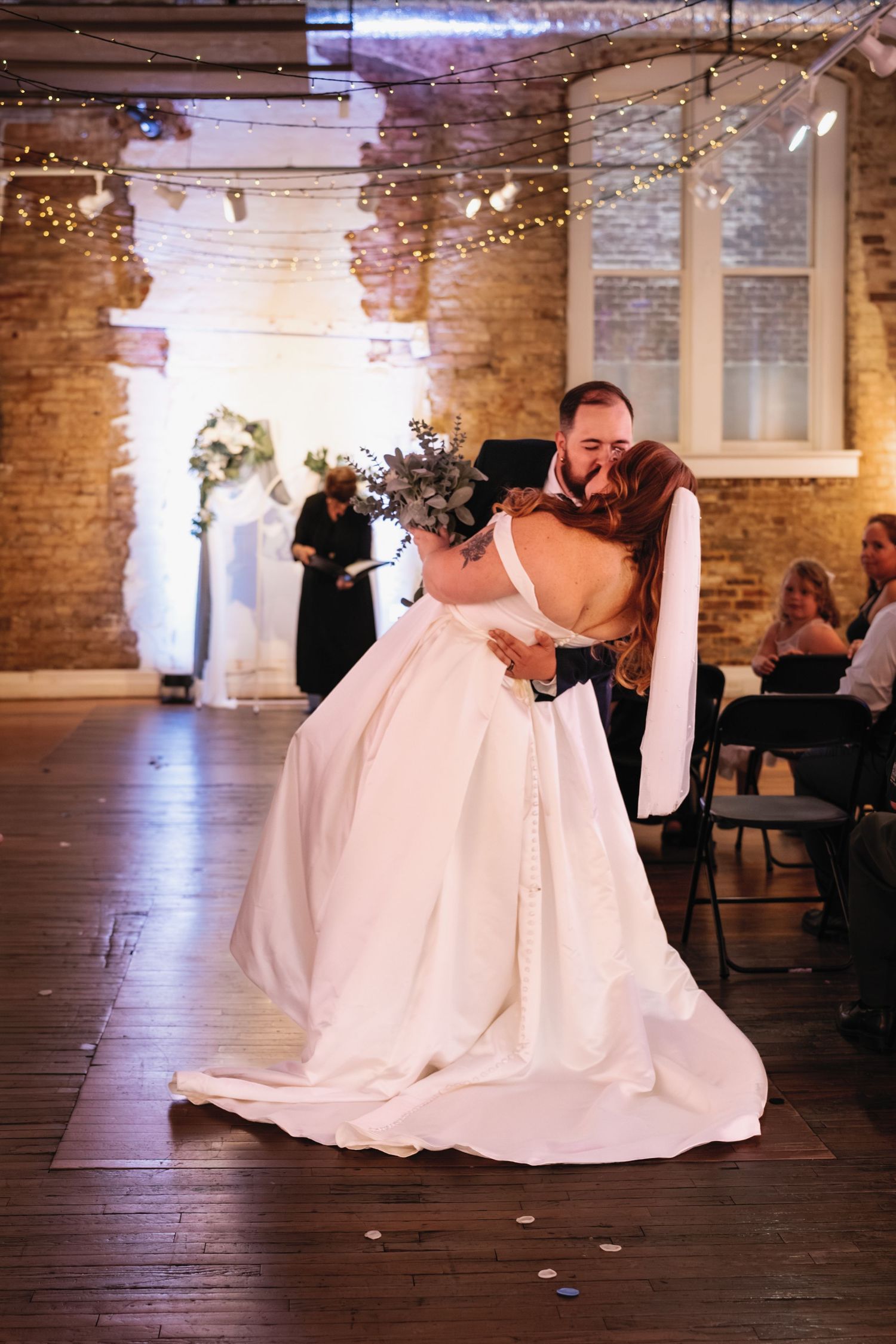 A romantic first dance at a wedding reception in a rustic brick venue decorated with twinkling lights.