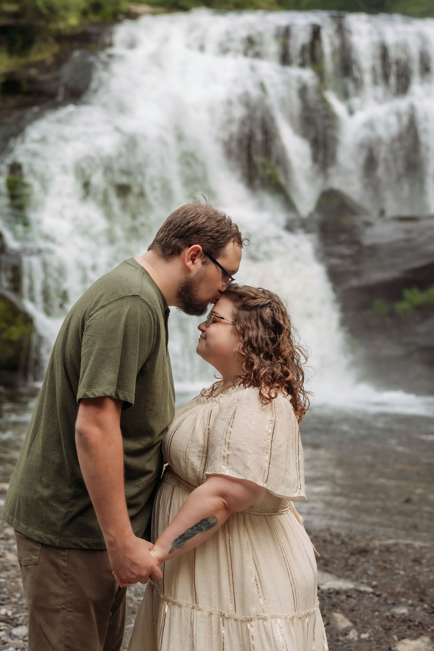 A romantic couple shares tender moments in front of a cascading waterfall on a misty afternoon.