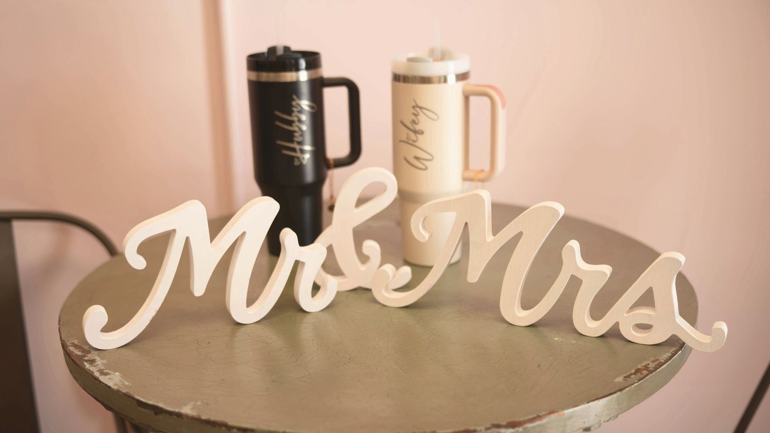 Black and white travel mugs with 'Mr & Mrs' wedding decor displayed on a round gray surface.