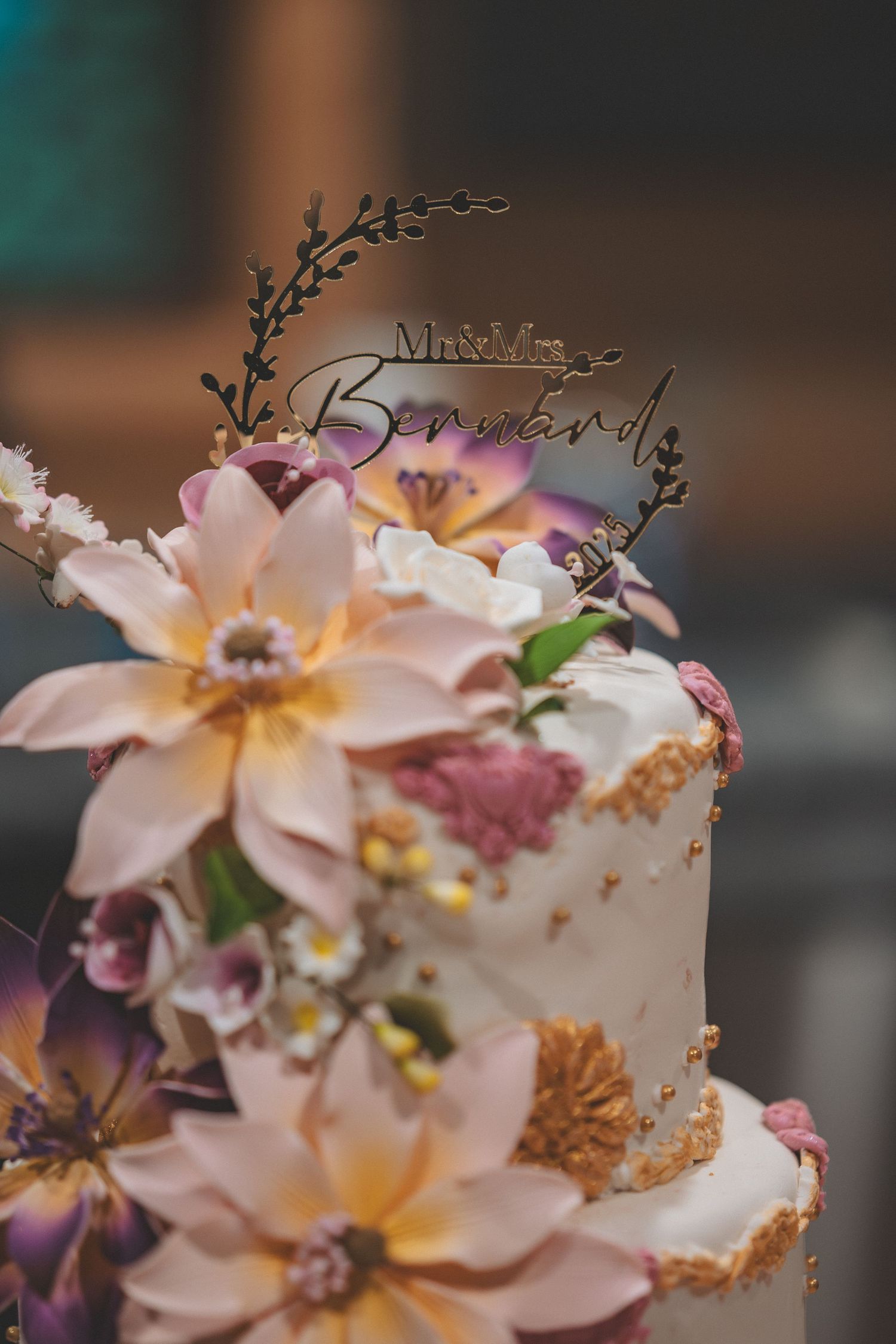 Delicate pink and purple floral wedding cake decorations with intricate gold accents on a soft-focused background.
