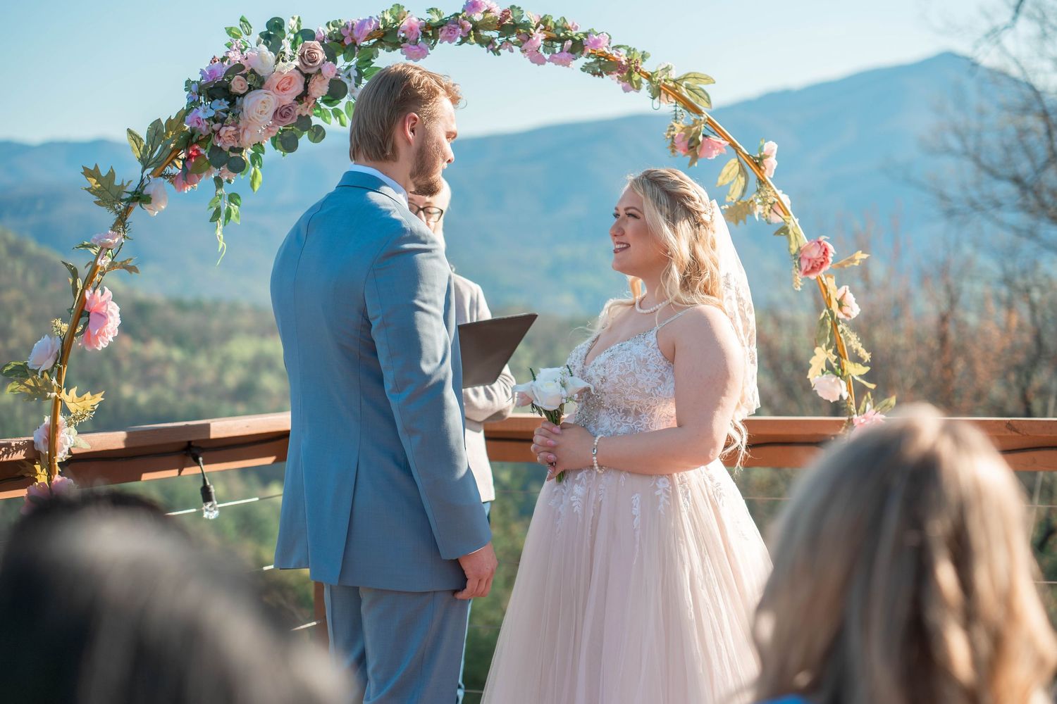 Outdoor wedding ceremony at mountain resort with floral arch and scenic mountain backdrop on sunny day.