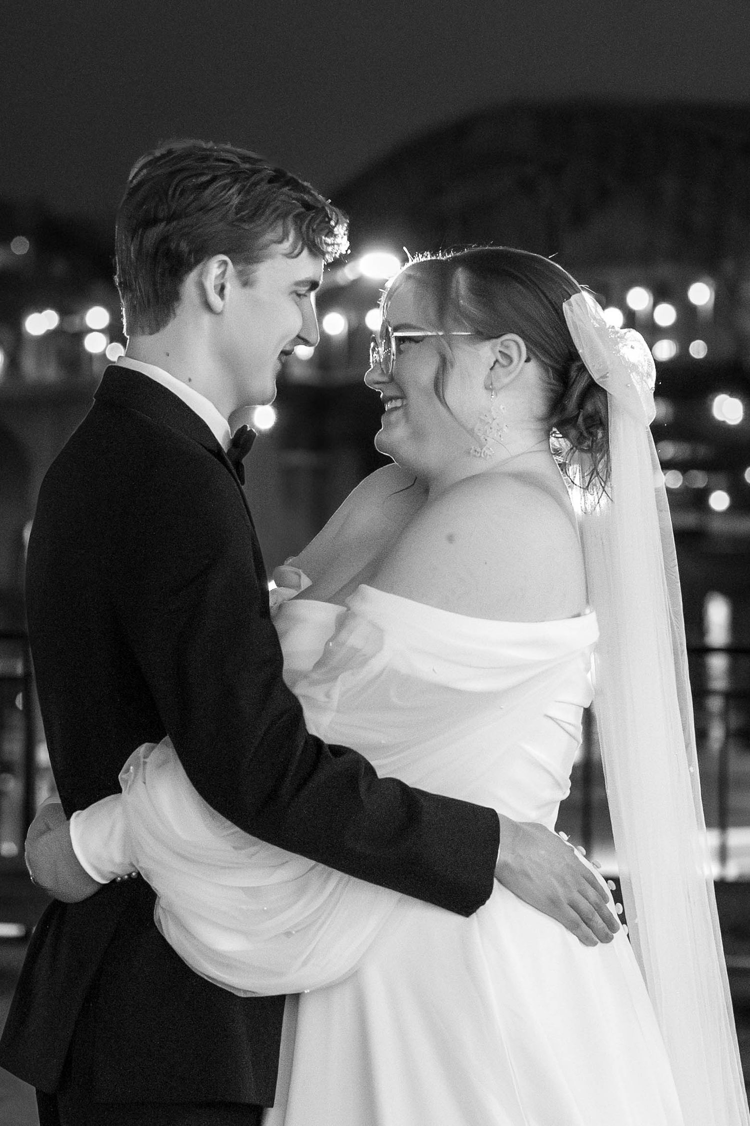 A romantic black and white portrait of a newlywed couple embracing during their nighttime wedding celebration.