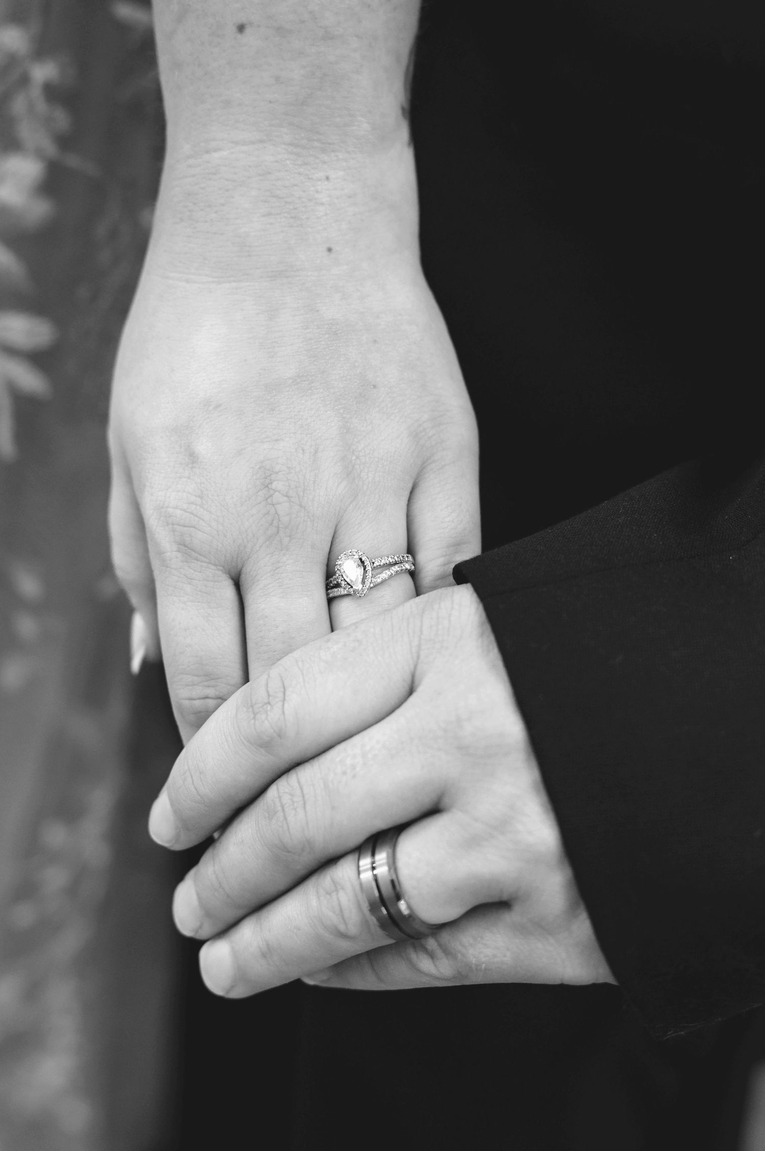 Black and white close-up of two hands with wedding rings showing a tender moment between newlyweds.