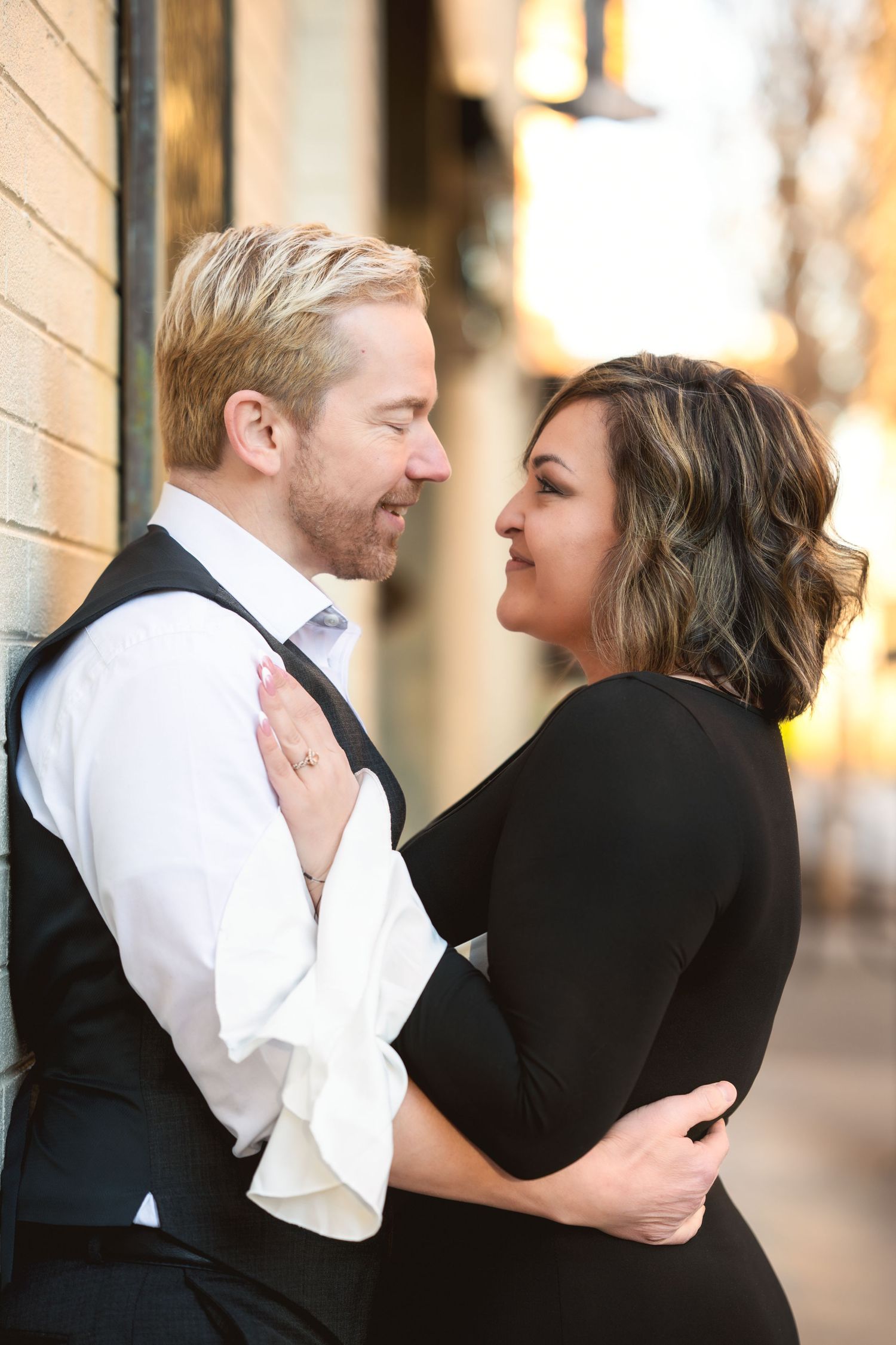 A romantic couple shares an intimate moment while embracing on a city sidewalk at sunset.