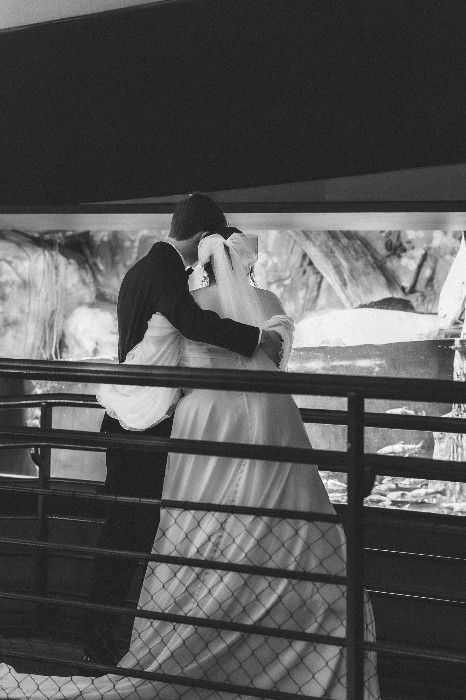 A black and white romantic moment captured of a couple embracing on a balcony with railing silhouettes.