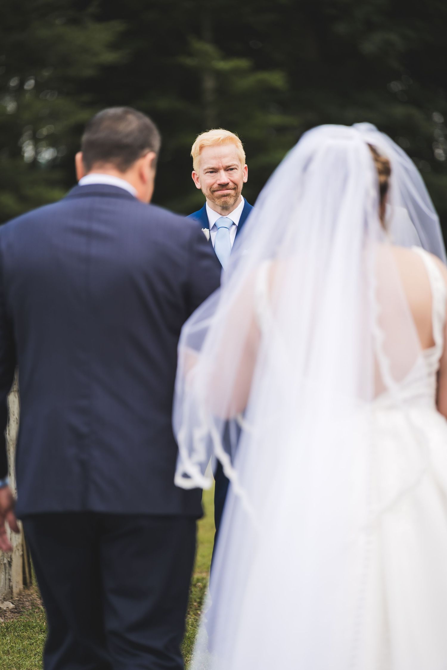 Groomsmen in navy suits stand sharing a candid moment during outdoor wedding.