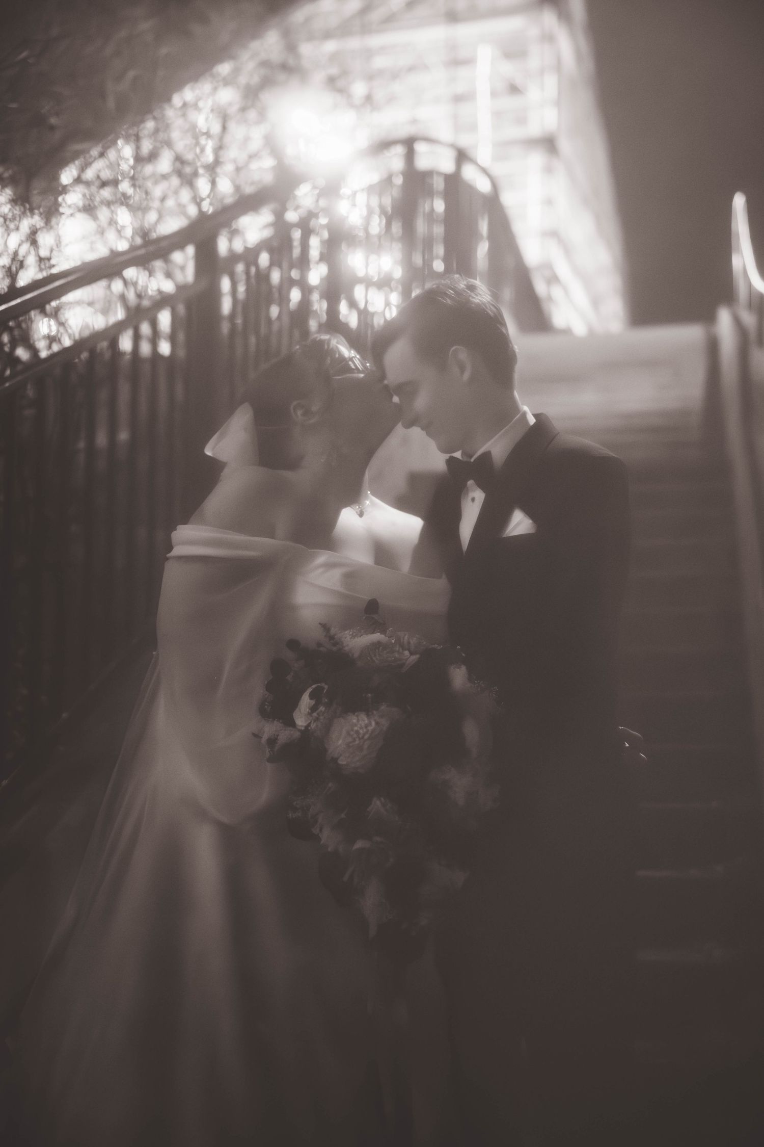 Romantic black and white portrait of newlyweds embracing on stairs with a soft dreamy effect.