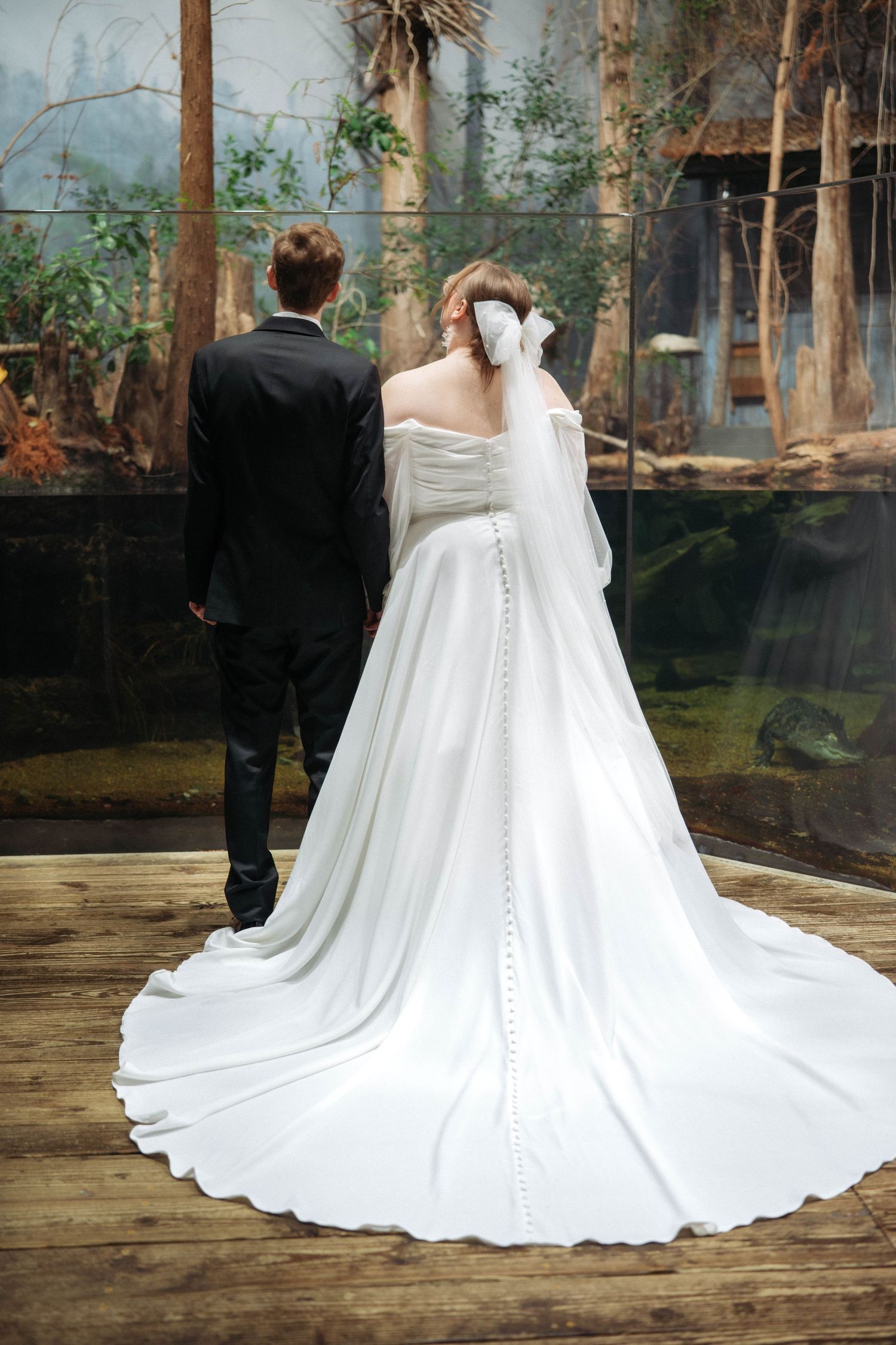 Detailed back view of a flowing white wedding dress with button details and cathedral train outdoors.