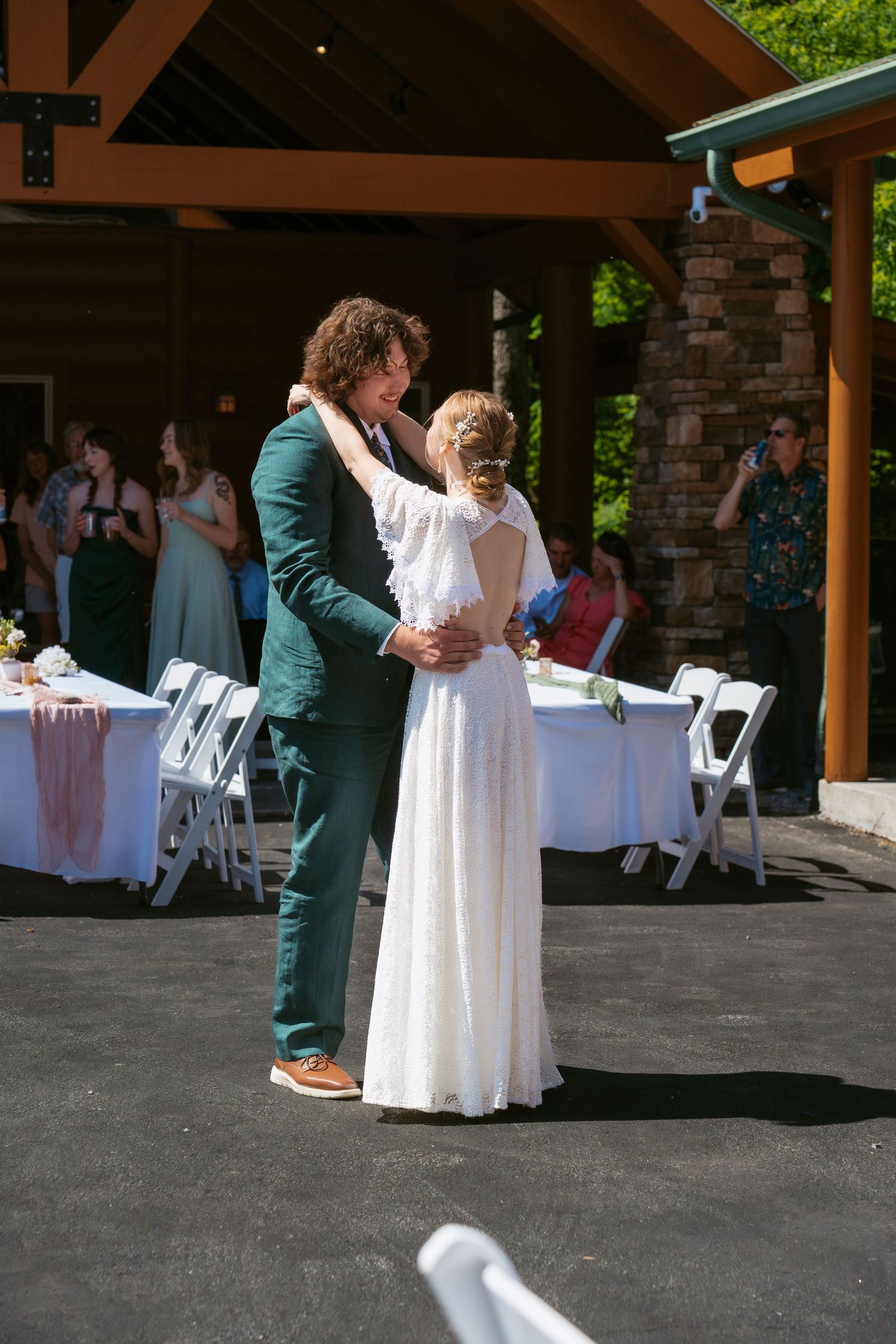 Two people in white and green formal attire dancing together at a covered outdoor venue with tables in background.
