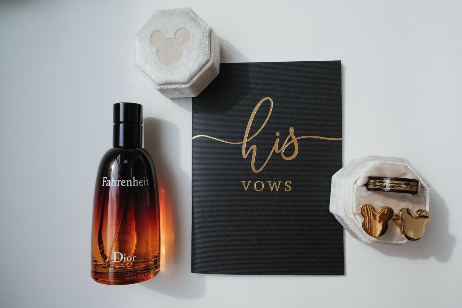 Wedding rings, vow book, perfume bottle, and delicate styling elements arranged in a romantic flat lay composition.