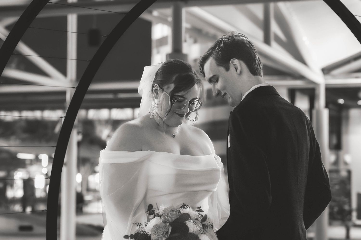 Intimate black and white portrait of newlyweds sharing a romantic moment under an arched structure.
