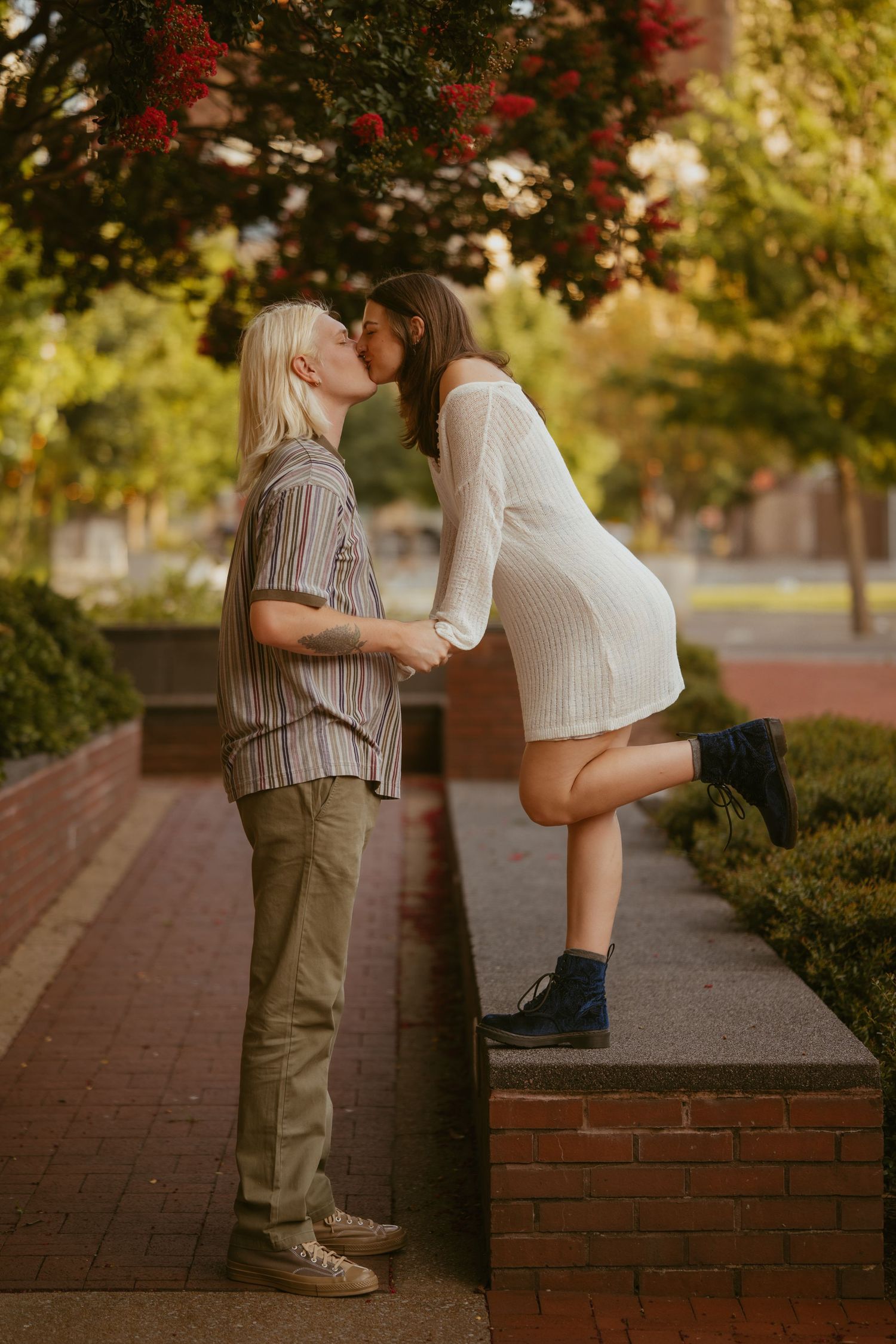 A romantic couple shares a tender moment on a brick ledge under autumn foliage at sunset.