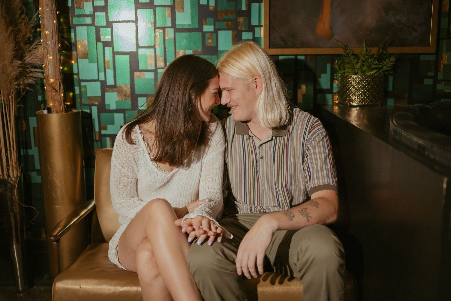 A couple shares an intimate moment in front of a turquoise mosaic wall at a dimly lit venue.