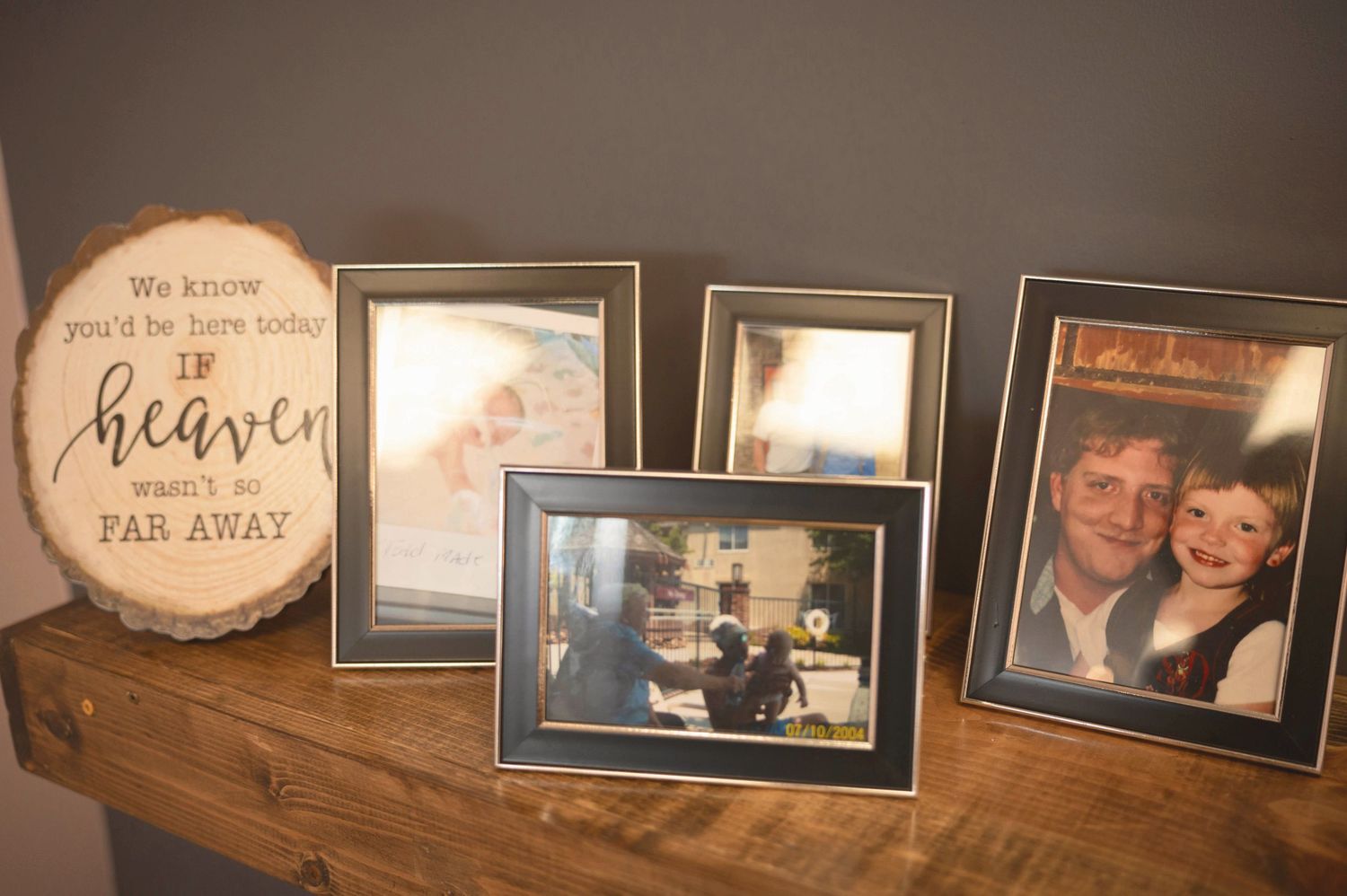 Framed photographs and decorative sign reading 'Heaven' displayed on wooden shelf with sentimental family memories.