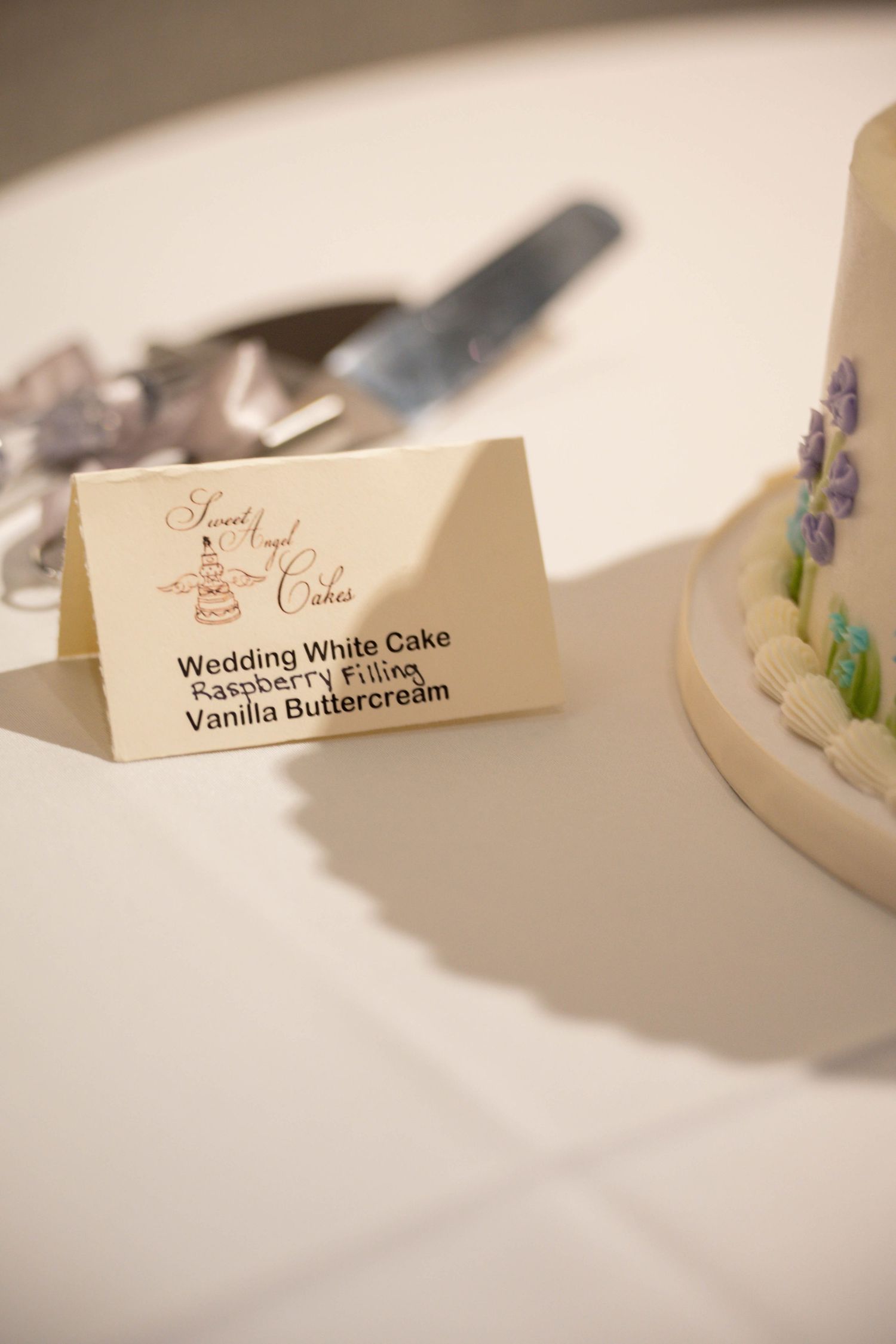 Wedding cake flavor card displays 'Wedding White Cake with Vanilla Buttercream' on a white tablecloth.