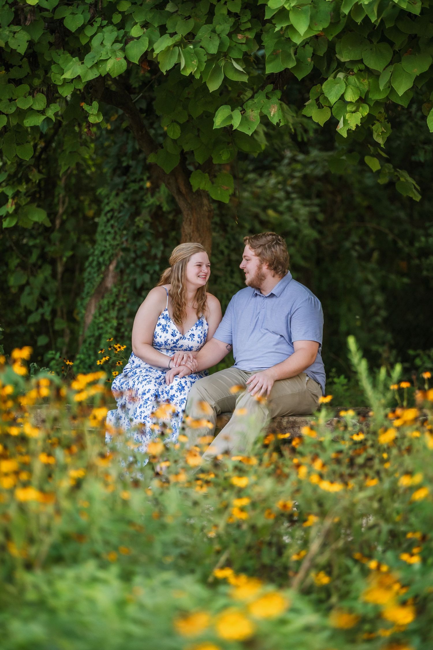 A couple sits together in a garden surrounded by vibrant yellow flowers and lush green foliage.