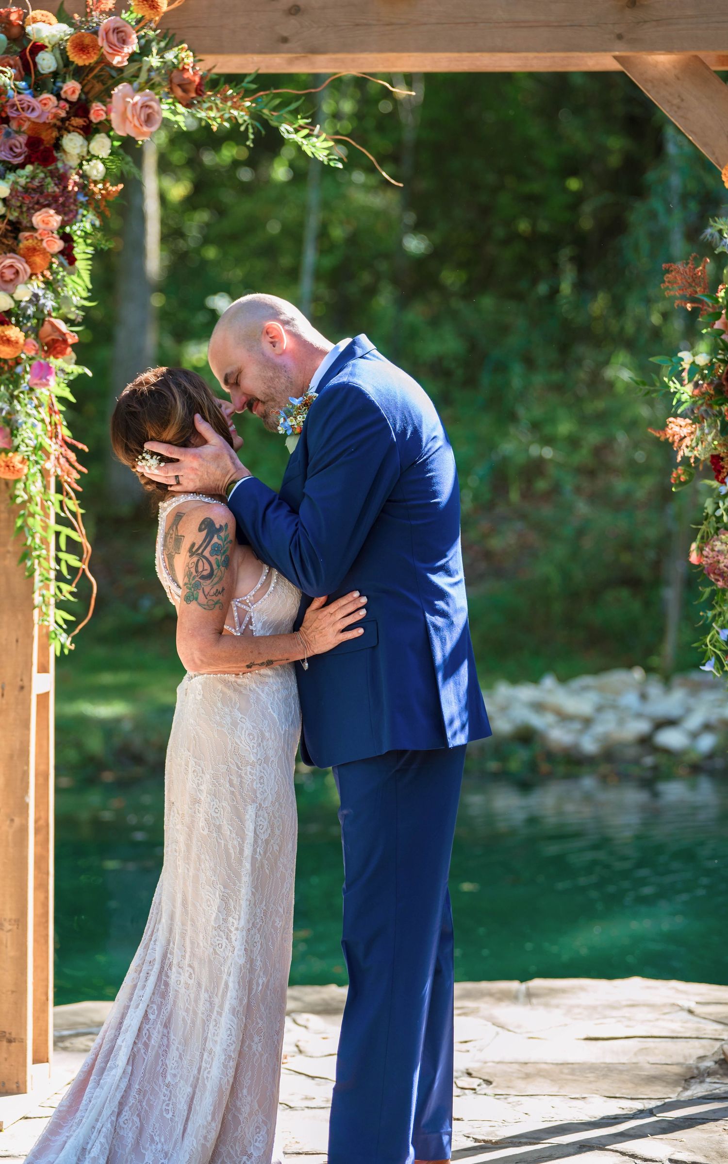 A romantic wedding moment under a wooden pergola decorated with colorful flowers.