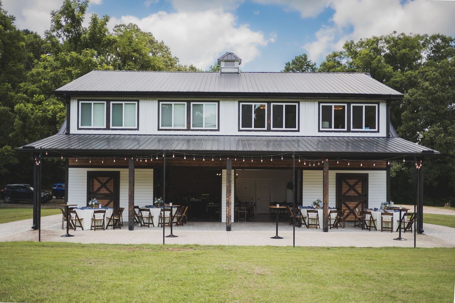 Long white horse barn with overhanging roof and outdoor seating areas in a serene country setting.