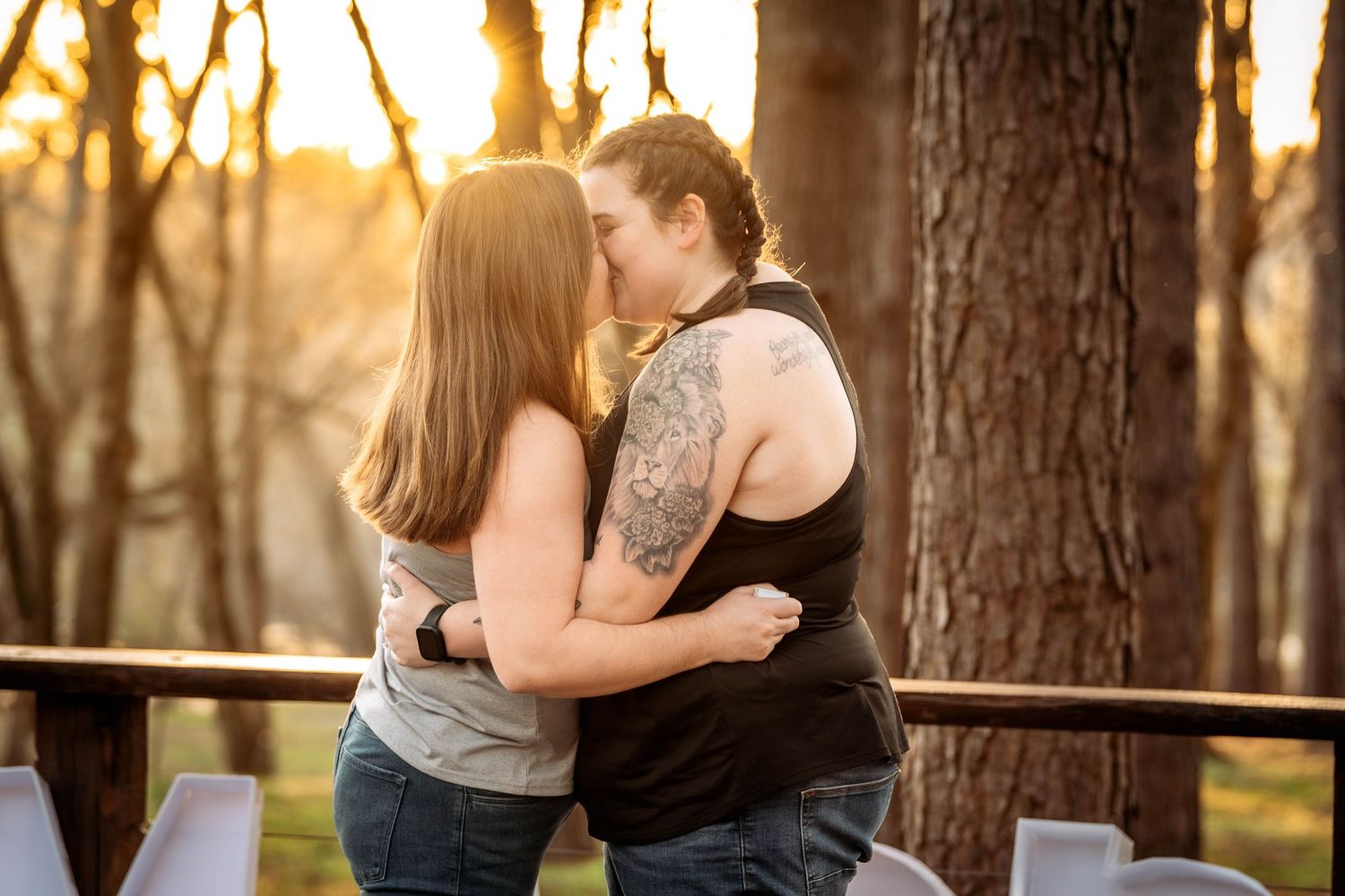 Romantic couple embraces in warm golden sunlight filtering through trees in a forest setting during sunset.
