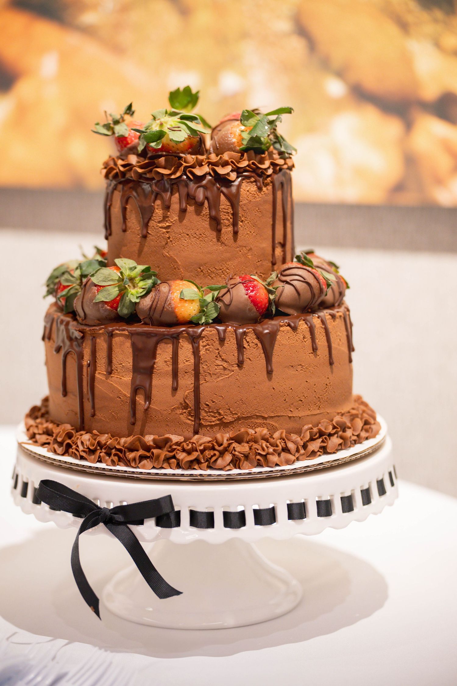 A two-tier chocolate drip wedding cake decorated with chocolate-covered strawberries and ganache.