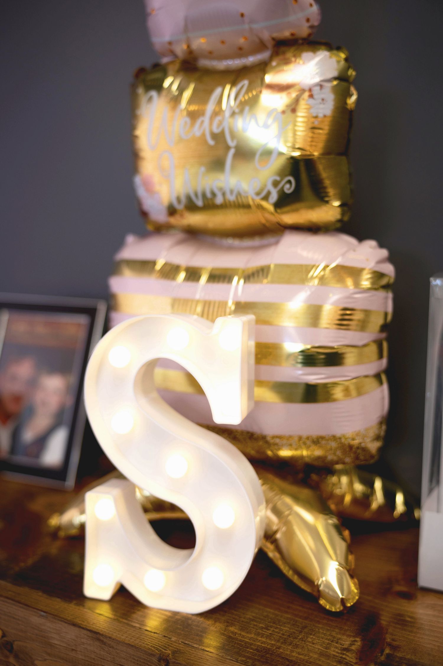 An illuminated white letter S with gold metallic balloons and party decorations on a wooden surface.