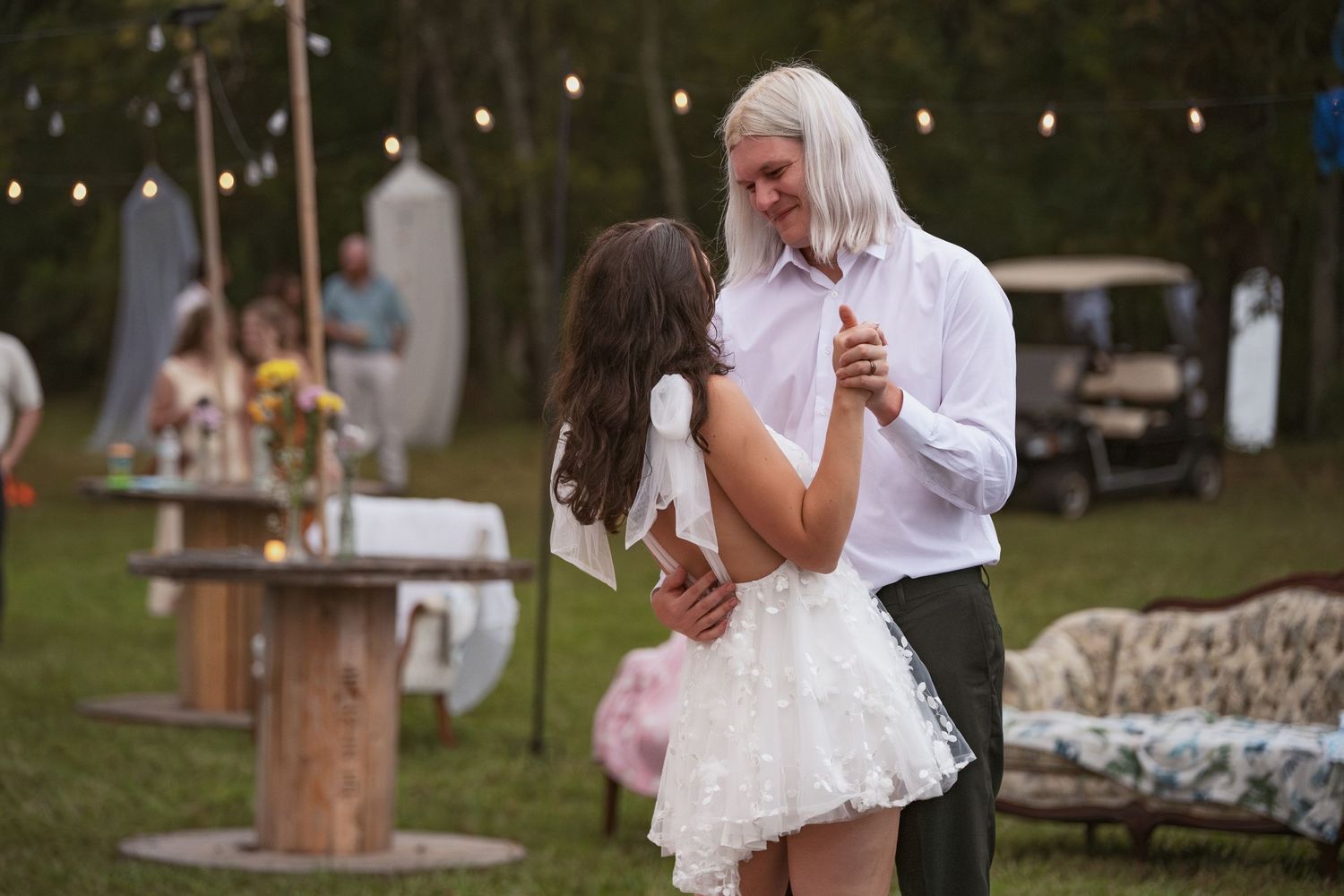 Wedding reception guests mingle under outdoor string lights at a rustic garden venue during sunset.