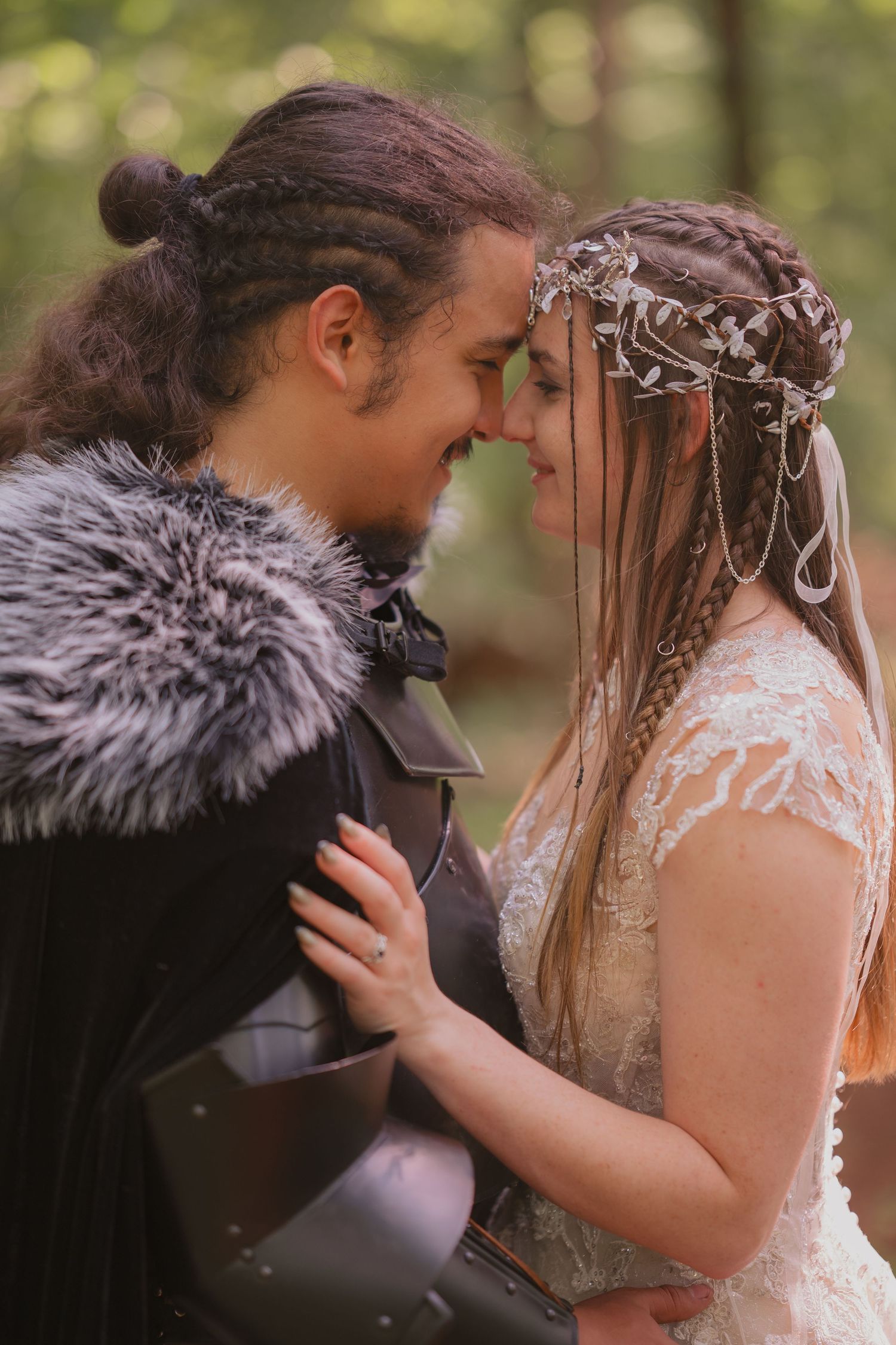 A romantic couple in medieval fantasy costumes share an intimate moment together in a forest setting.