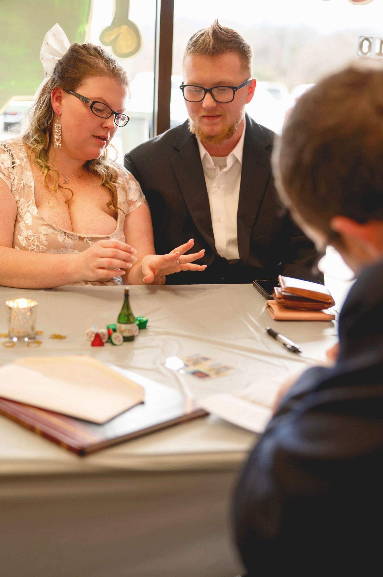 Couple in formal attire sits at a table reviewing documents and having a conversation with someone across from them.
