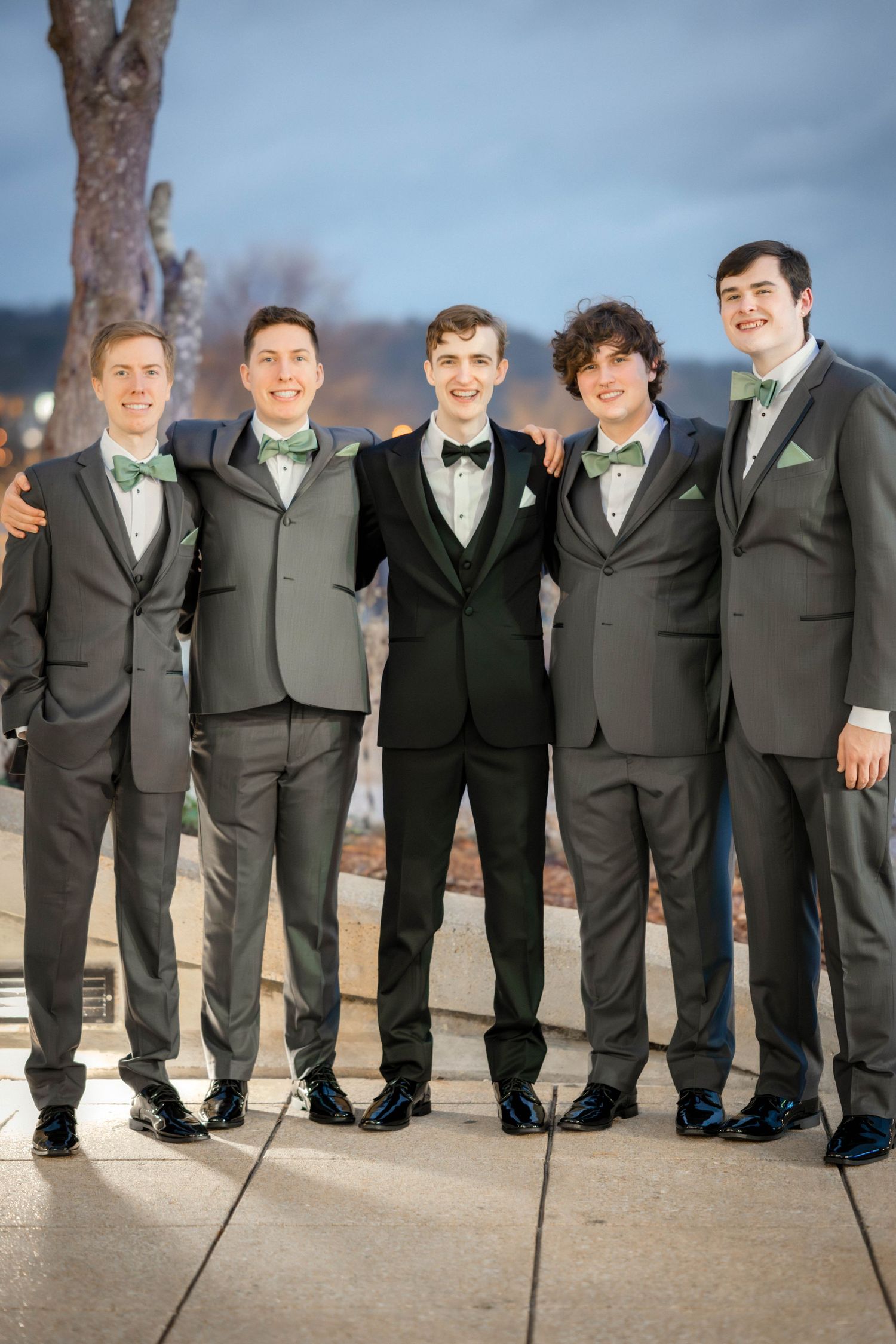 A group of five groomsmen stand together wearing matching grey and black tuxedos with mint green accessories.
