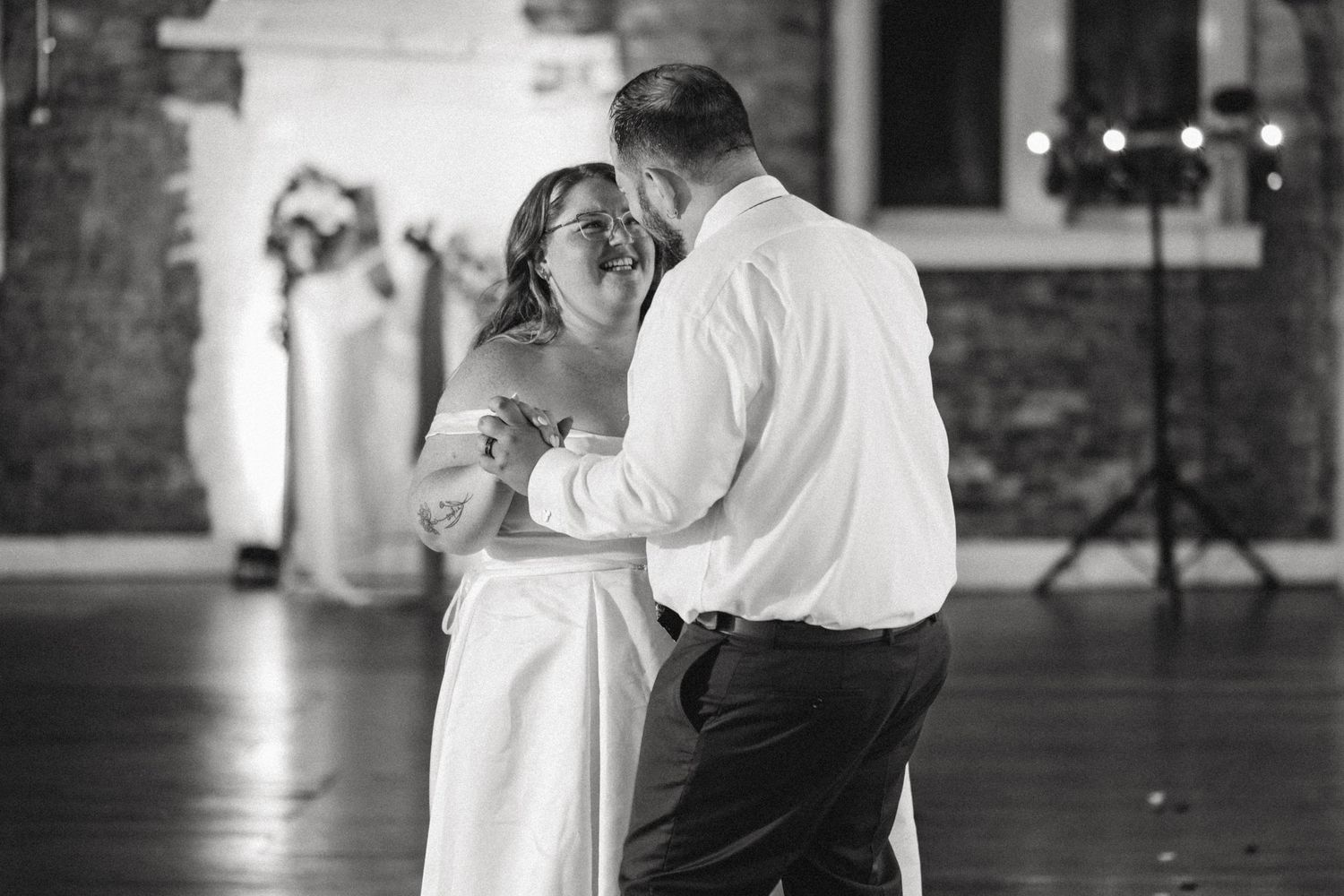 Two dancers in white and black attire perform a gentle ballroom dance in a dimly lit indoor space.