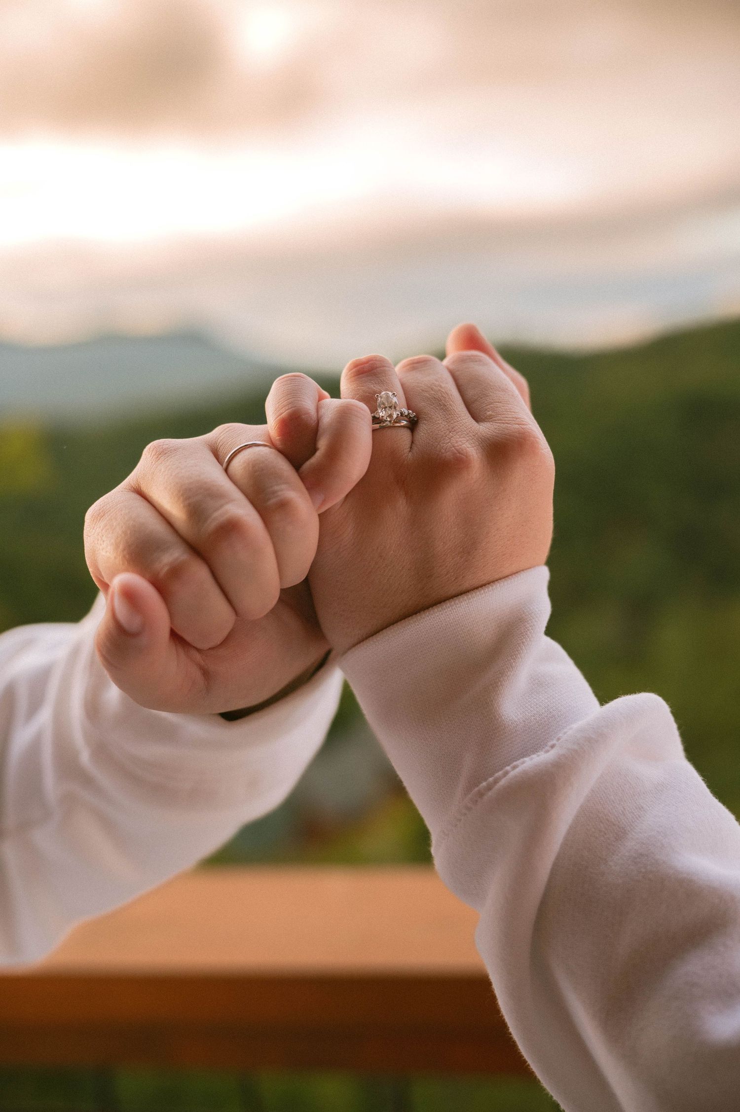 Two hands wearing white sleeves are interlocked in a pinky promise gesture against a blurred background.