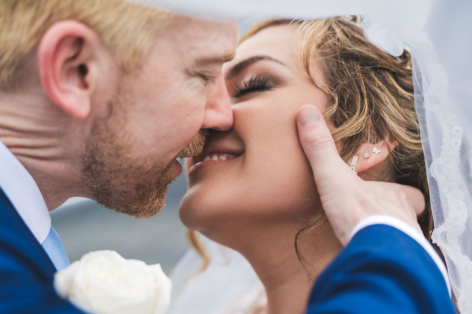 A romantic bridal couple sharing an intimate kiss against a light-filled outdoor background.