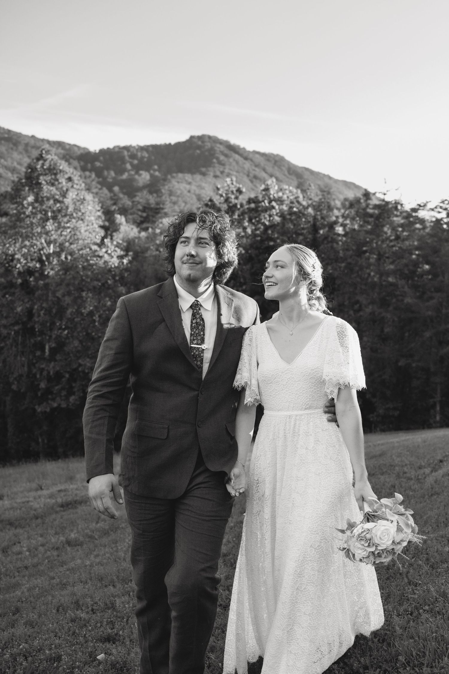 A romantic wedding couple poses together in a rustic outdoor mountain setting at sunset with trees in the background.
