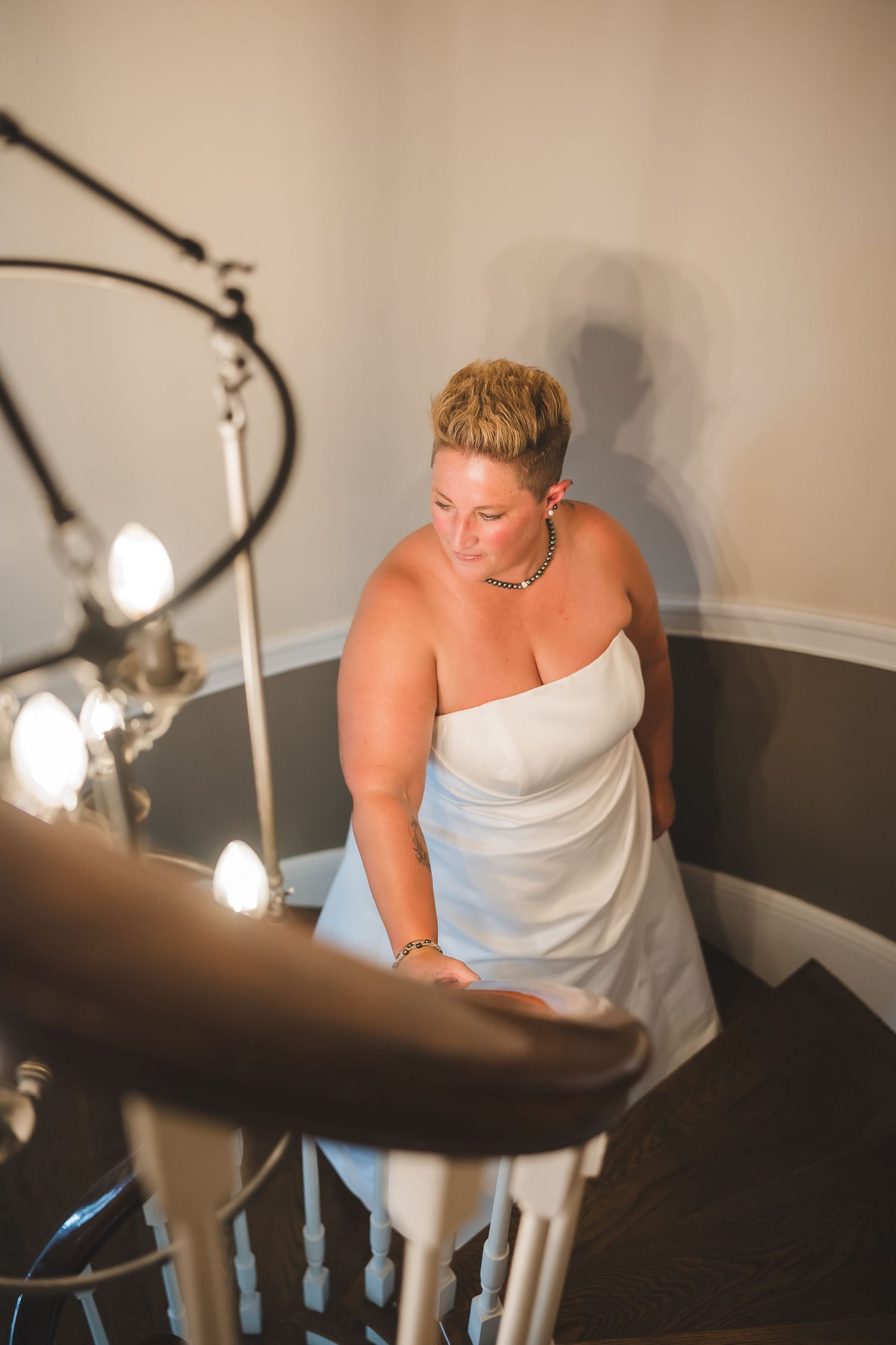 Someone in a white strapless dress walks down a curved staircase with dramatic spot lighting in the scene.
