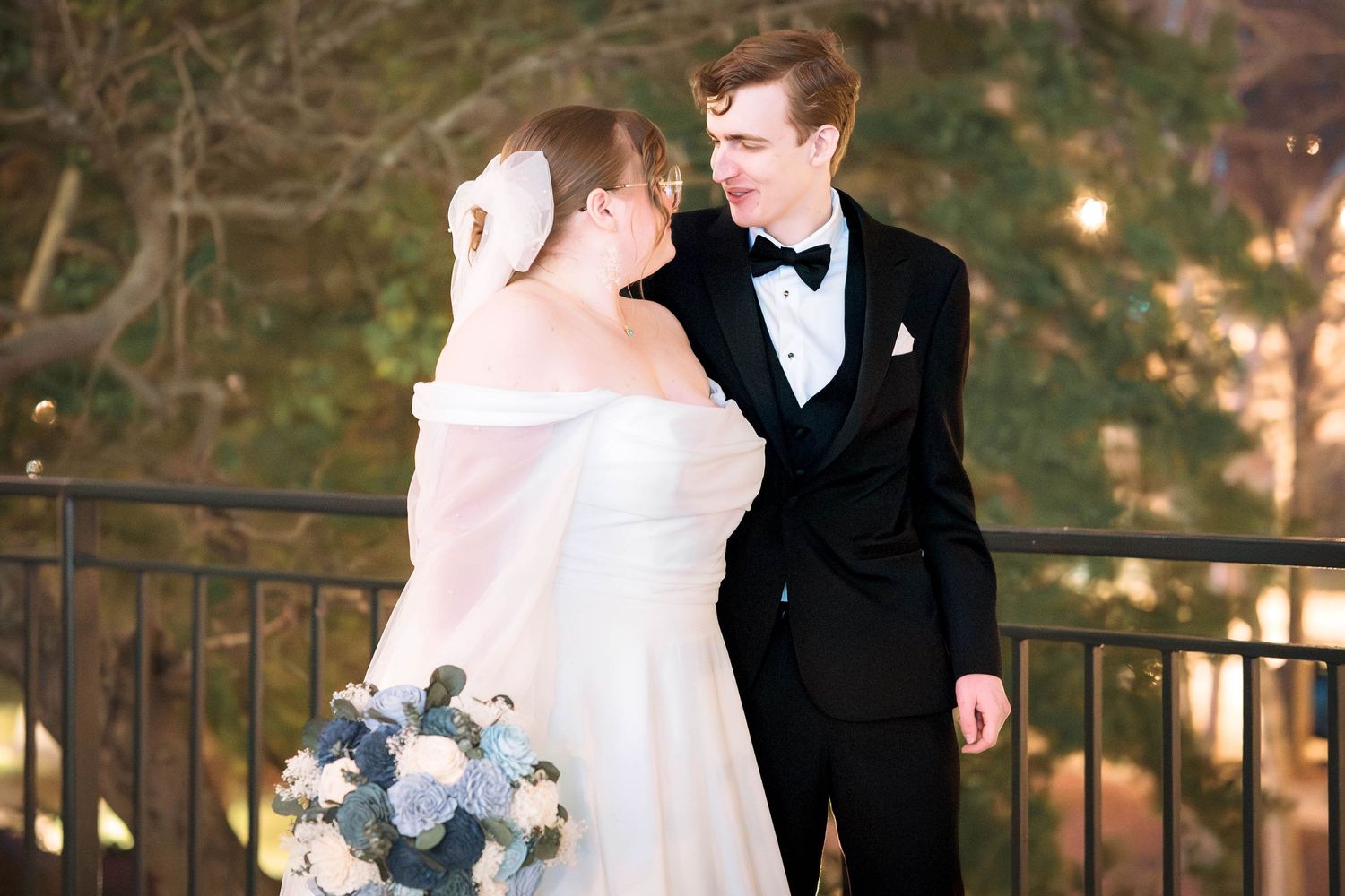 A romantic evening wedding portrait with a bouquet of blue and white flowers against a garden backdrop.