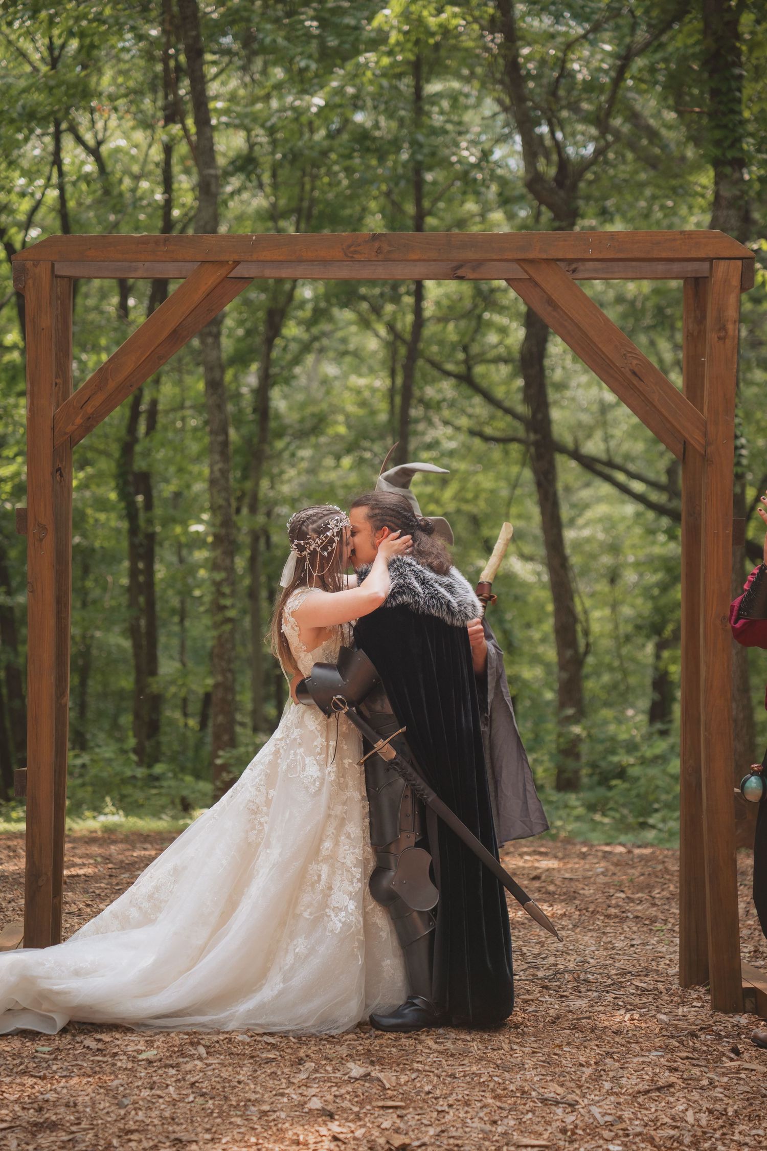 A couple dances together during a wedding photoshoot in a rustic wooden pergola surrounded by forest.