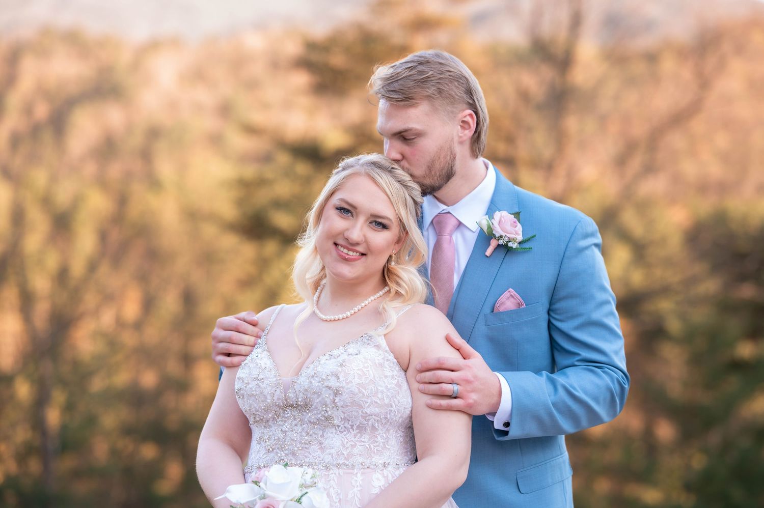A couple in formal wedding attire shares an intimate pose during an autumn outdoor photoshoot with golden lighting.