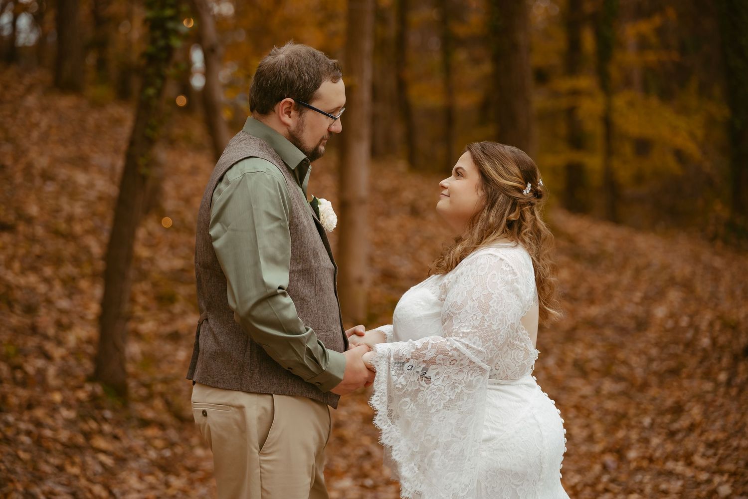 A couple in autumn wedding attire shares intimate moments among fallen leaves in a forest setting.