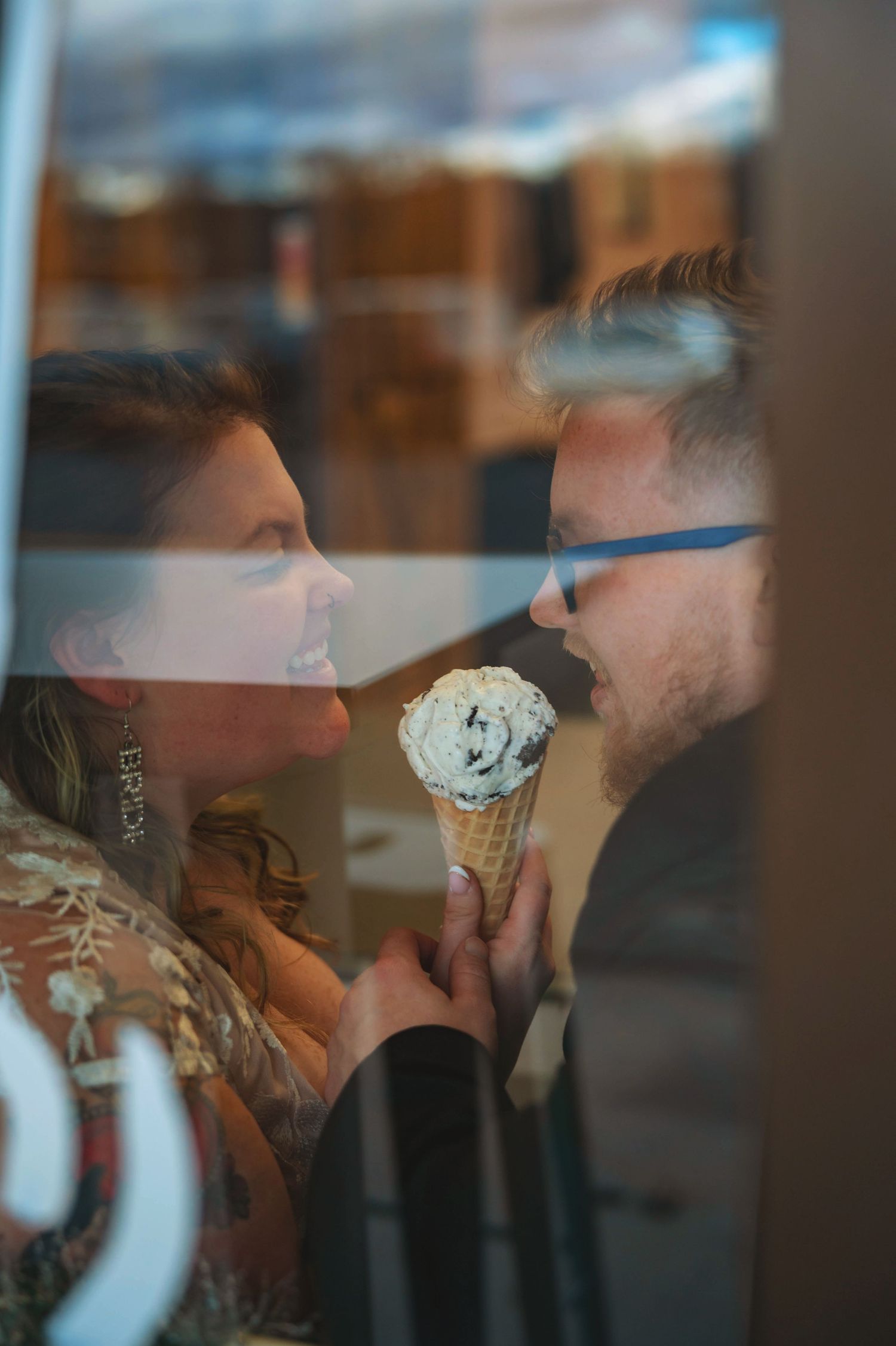 Couple sharing an ice cream cone together through window reflection.