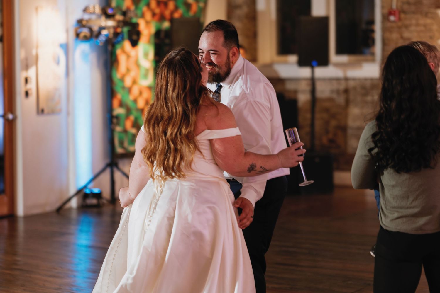 Multiple wedding guests dance and celebrate in a rustic brick-walled venue with warm lighting.