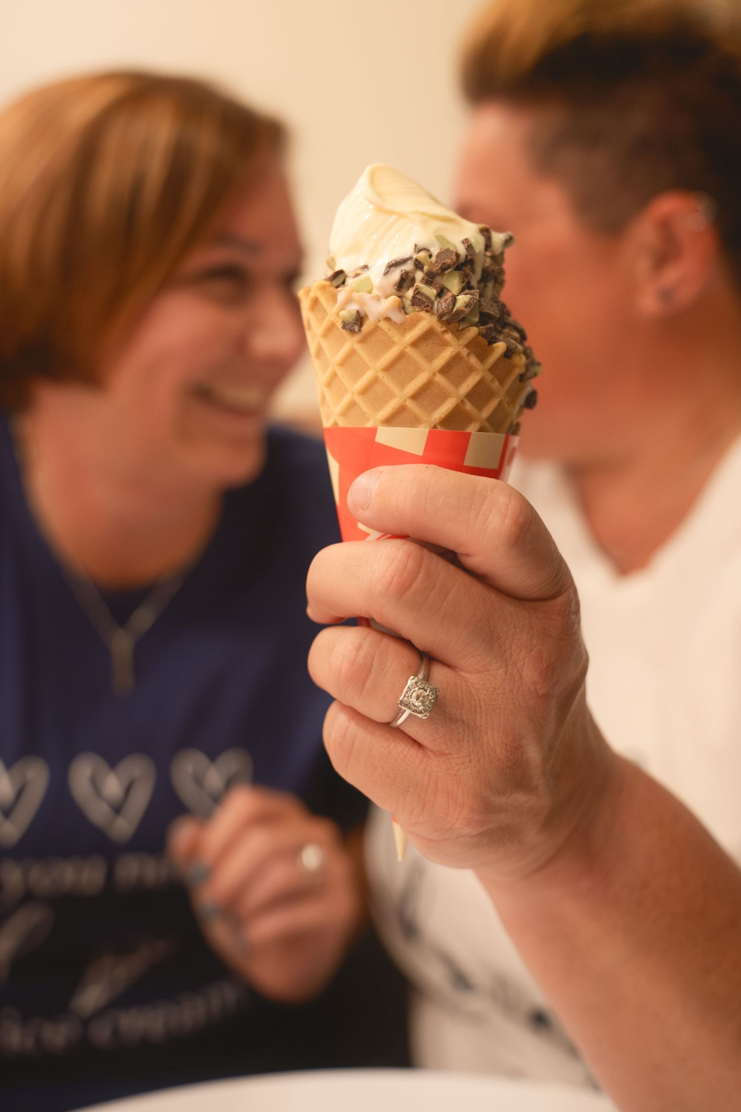 Hand holding a waffle cone with soft-serve ice cream topped with chocolate sprinkles while wearing a ring.
