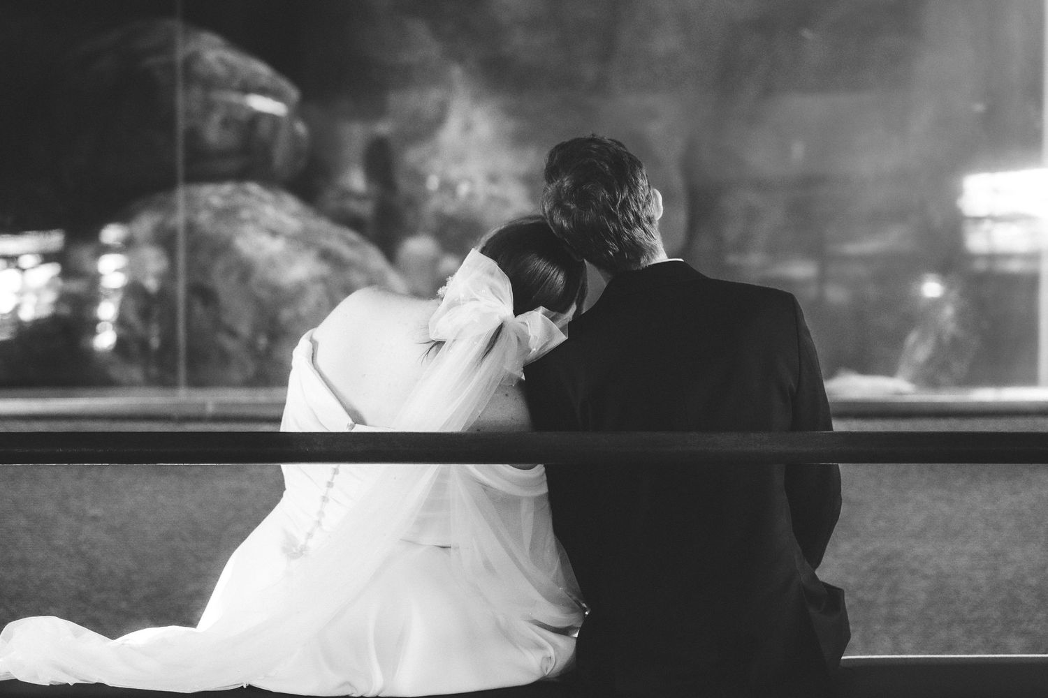 A black and white wedding photograph showing a couple sharing an intimate moment by a window at night.